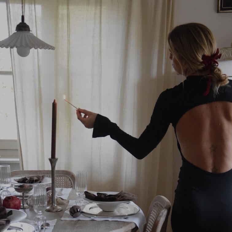 Femme en robe noire dos nu allumant une bougie sur une table élégamment dressée dans une salle à manger