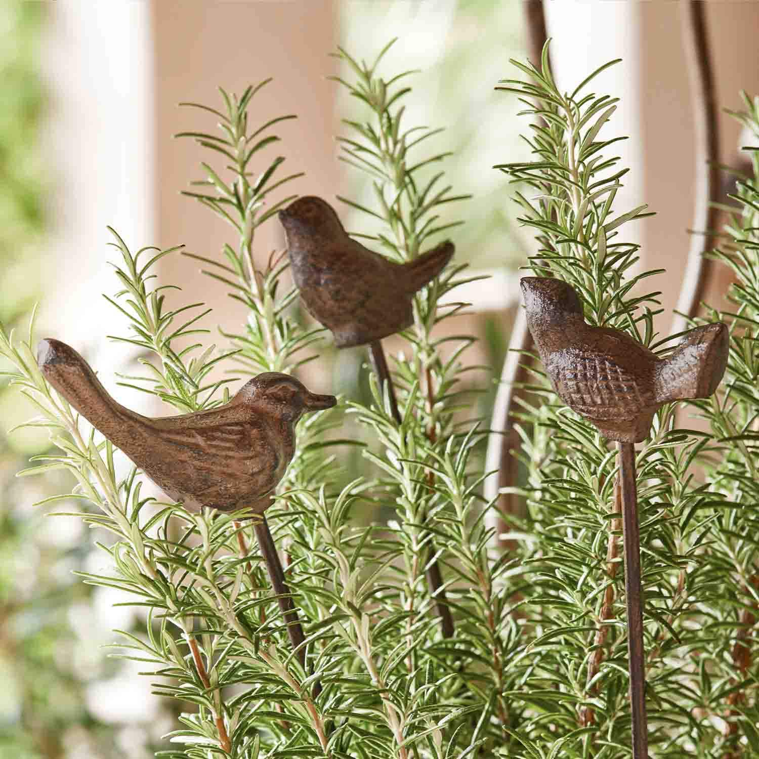 Oiseaux décoratifs en métal brun sur tiges plantés dans des branches vertes de romarin