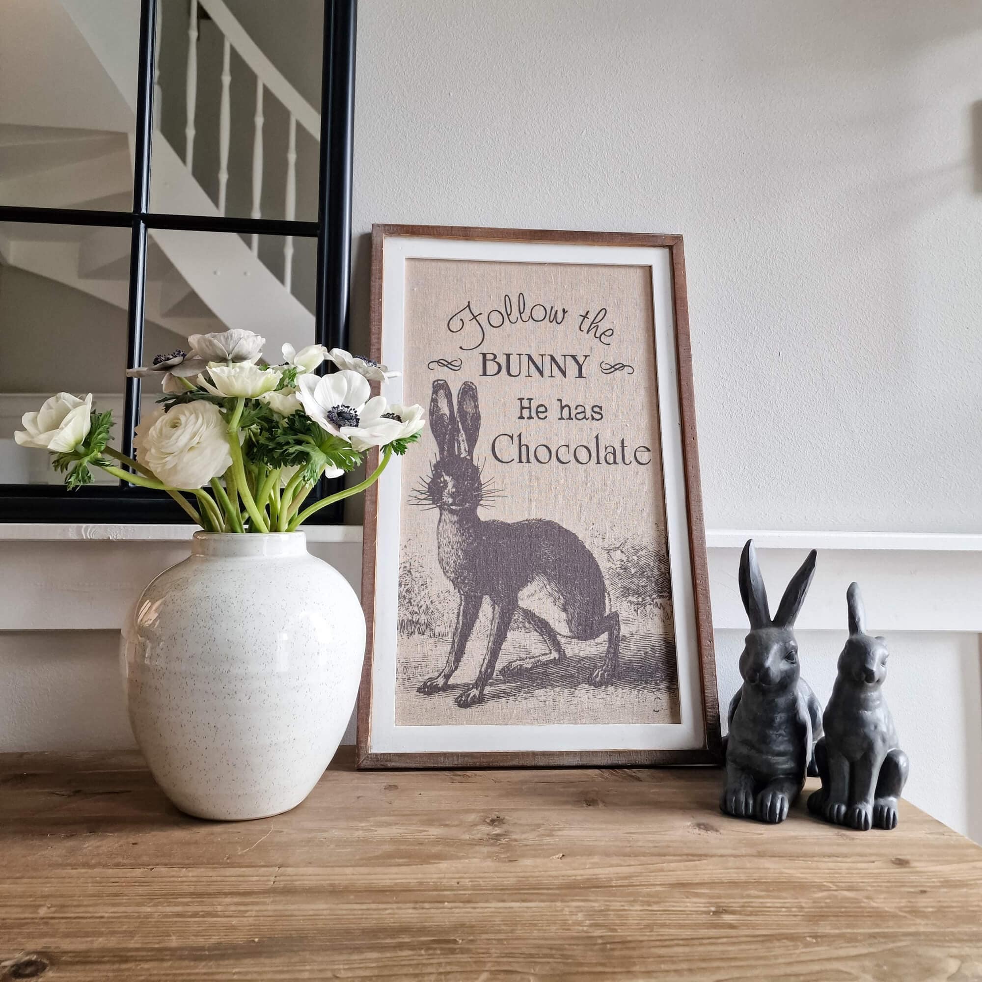 Tableau décoratif avec lapin et texte, fleurs blanches en vase en céramique, deux figurines de lapins sur table en bois
