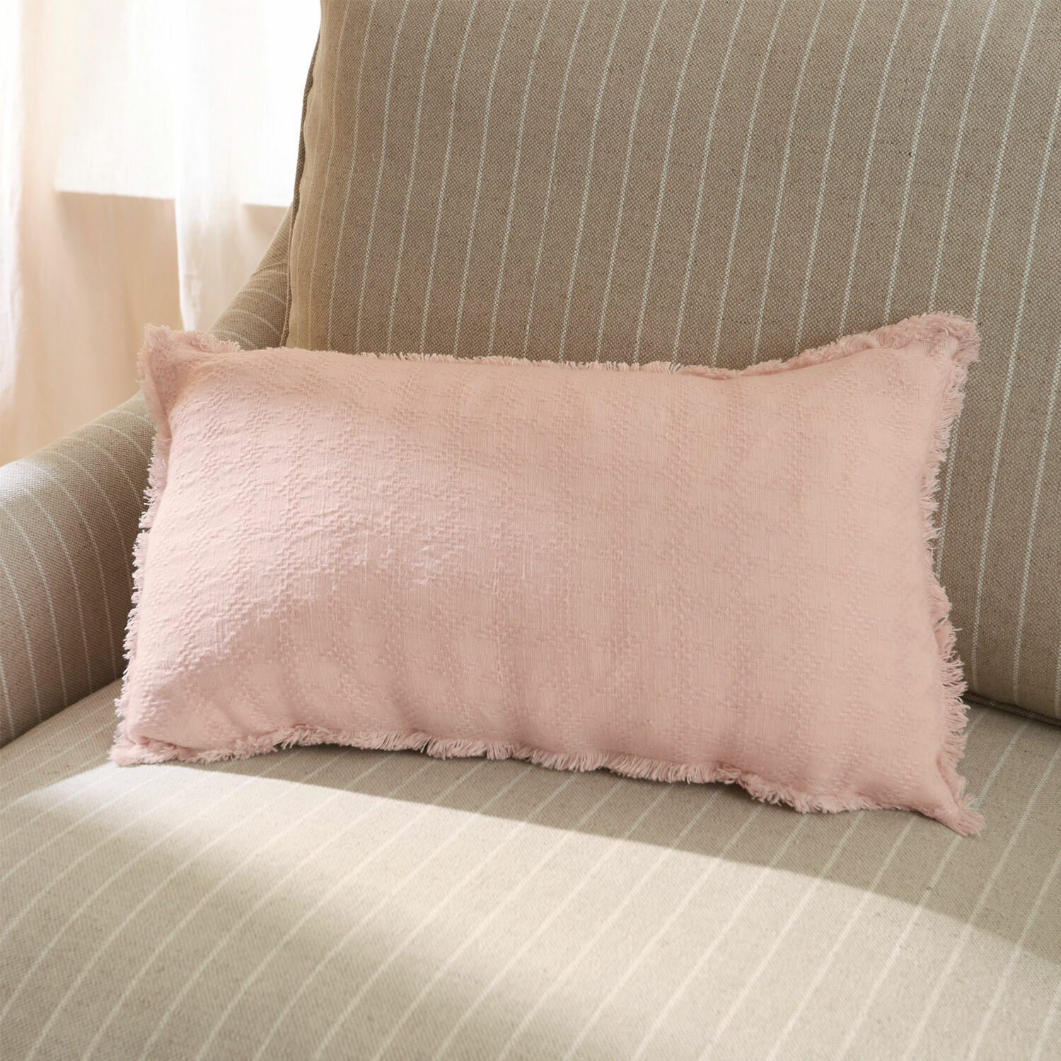 Housse de coussin Saavreda Coussin décoratif rose en tissu doux sur un canapé beige rayé, ambiance salon cosy