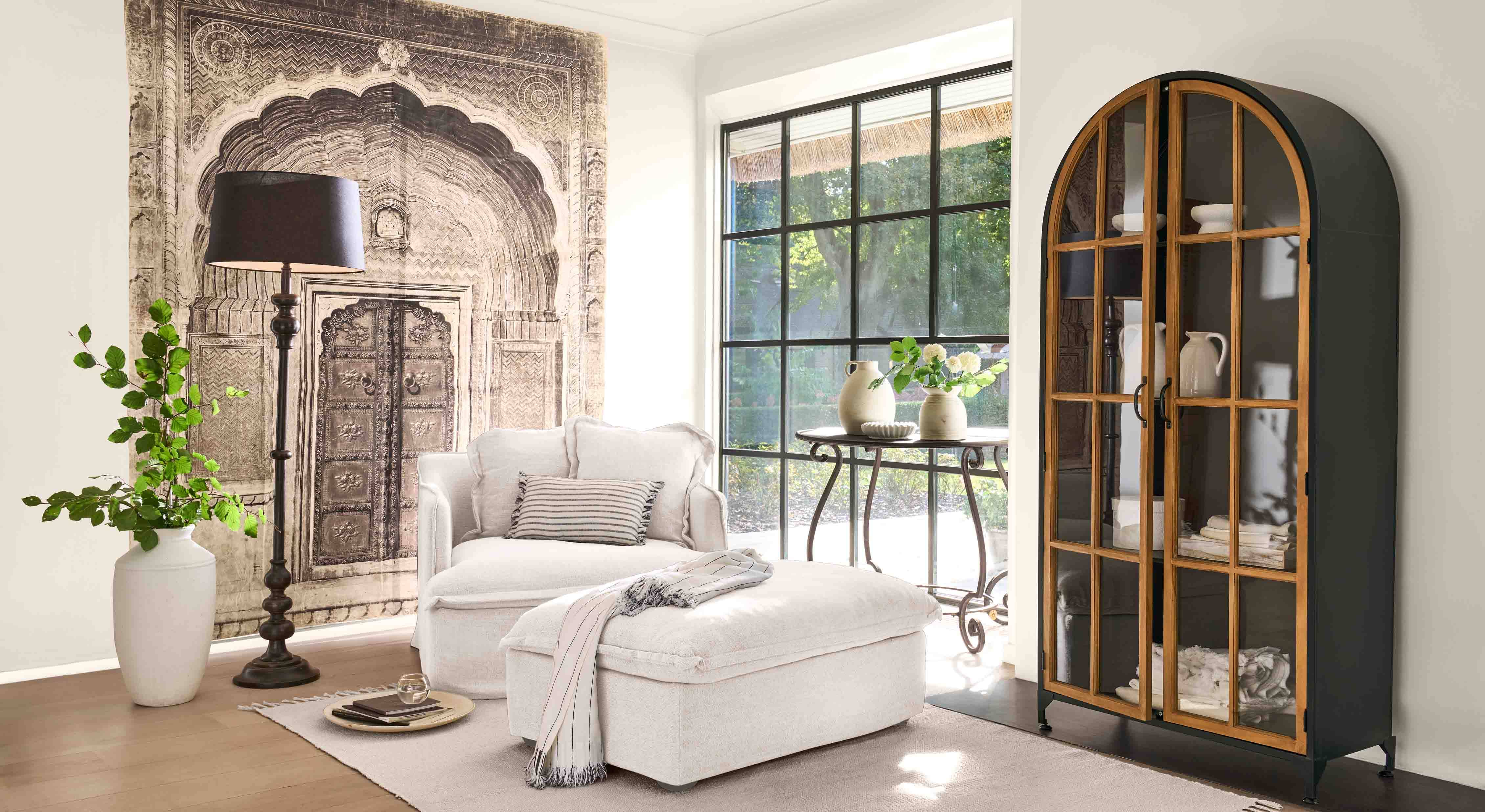 Fauteuil blanc confortable avec repose-pieds et lampe noire dans un salon lumineux avec vitrine décorative