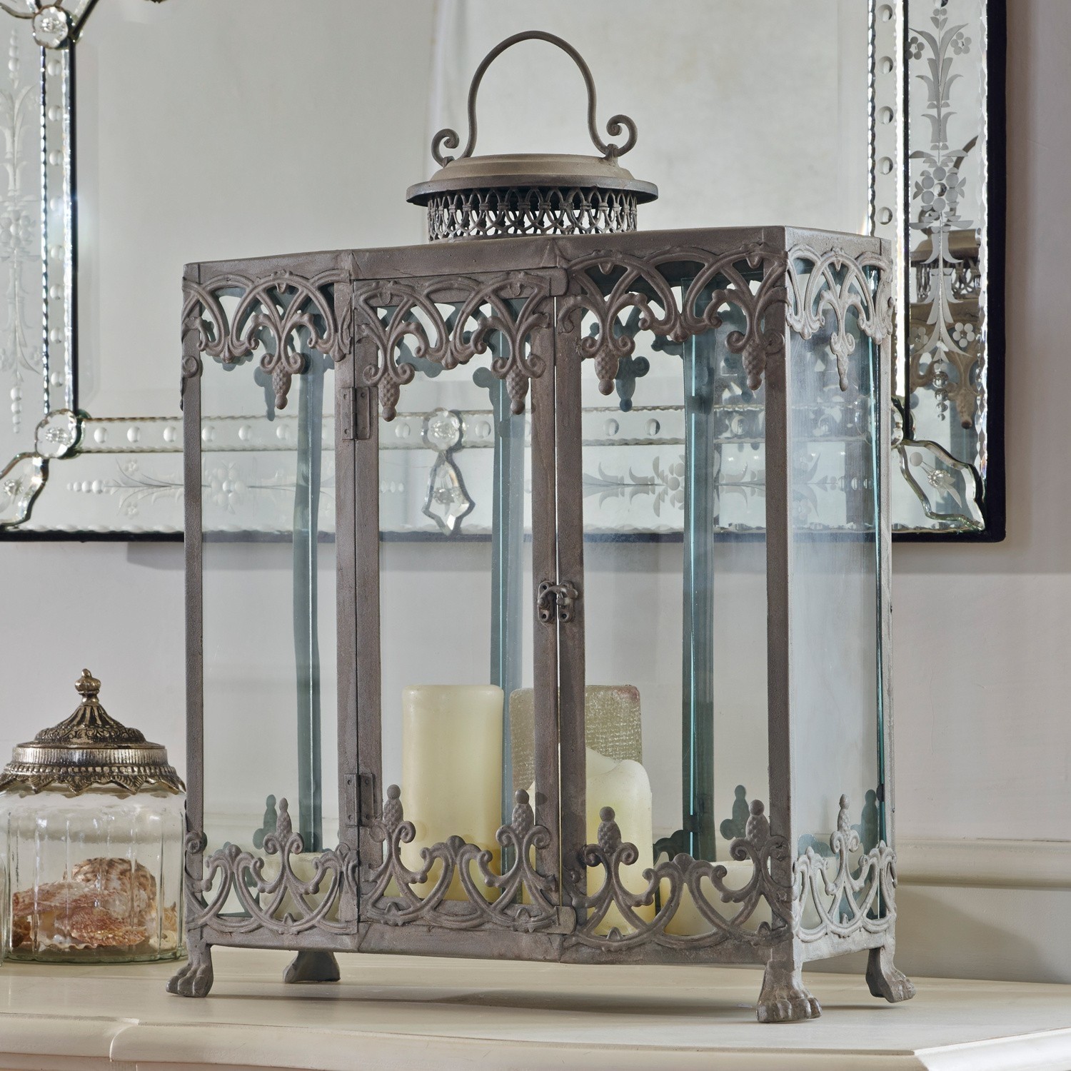 Lanterne Canousse Lanterne décorative en métal avec panneaux en verre et bougies crème posée sur une table