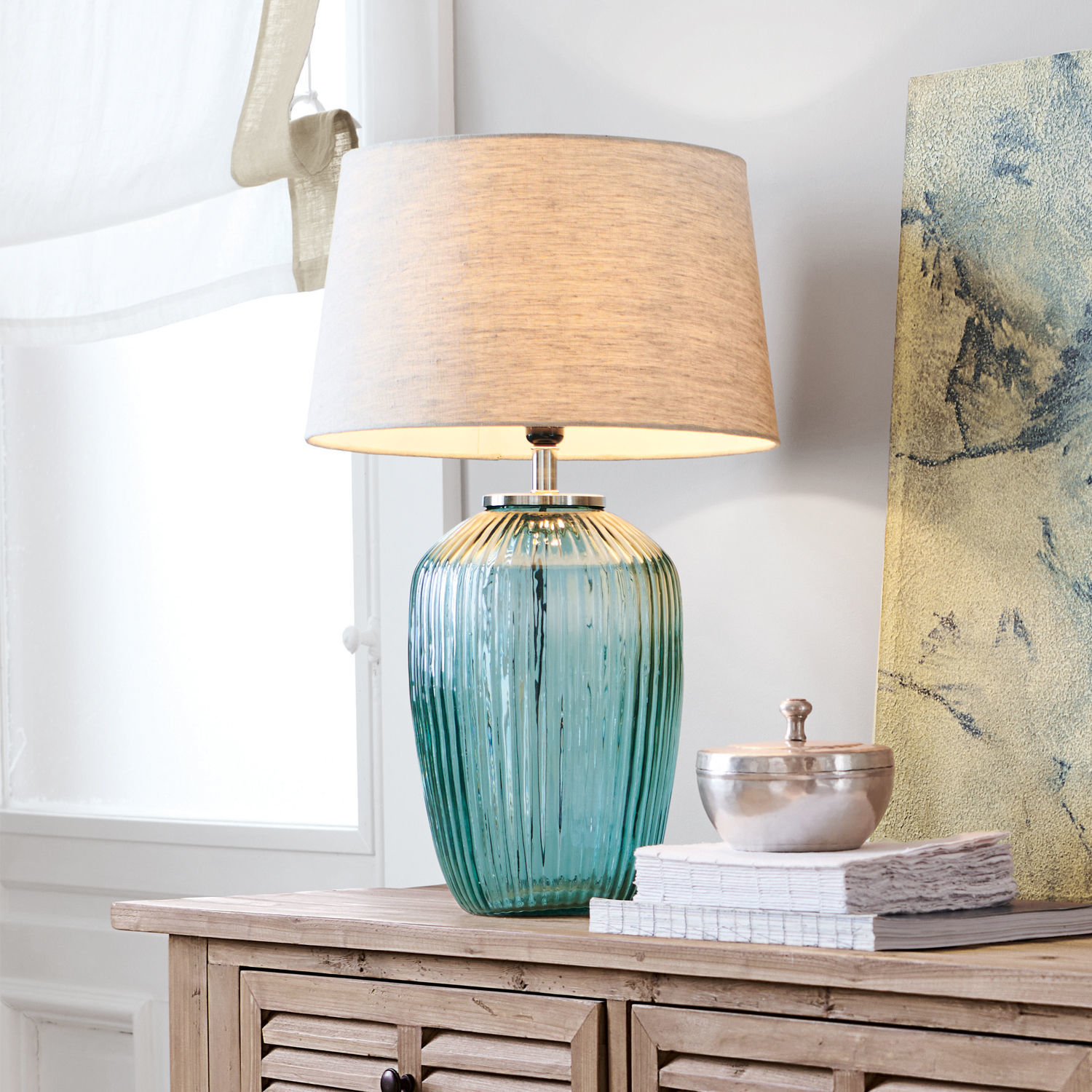 Lampe à poser Fenis Lampe de table en verre vert avec abat-jour beige posée sur un meuble en bois clair