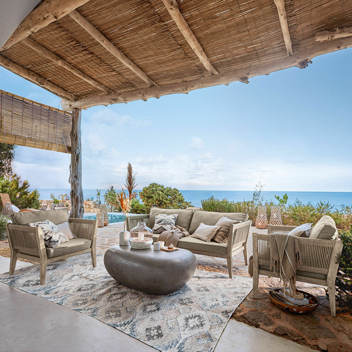 Salon de jardin FSC®-100% Biarritz Ensemble de mobilier de jardin beige avec table basse en béton sous un toit en bois face à la mer