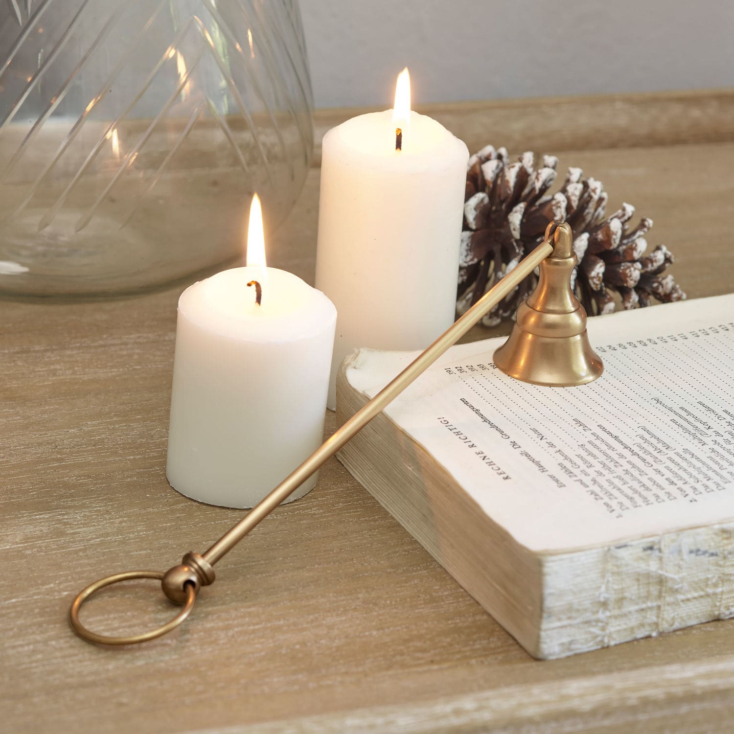 Éteignoir à bougies Perret Éteignoir à bougie en laiton sur table en bois avec bougies blanches allumées et pomme de pin