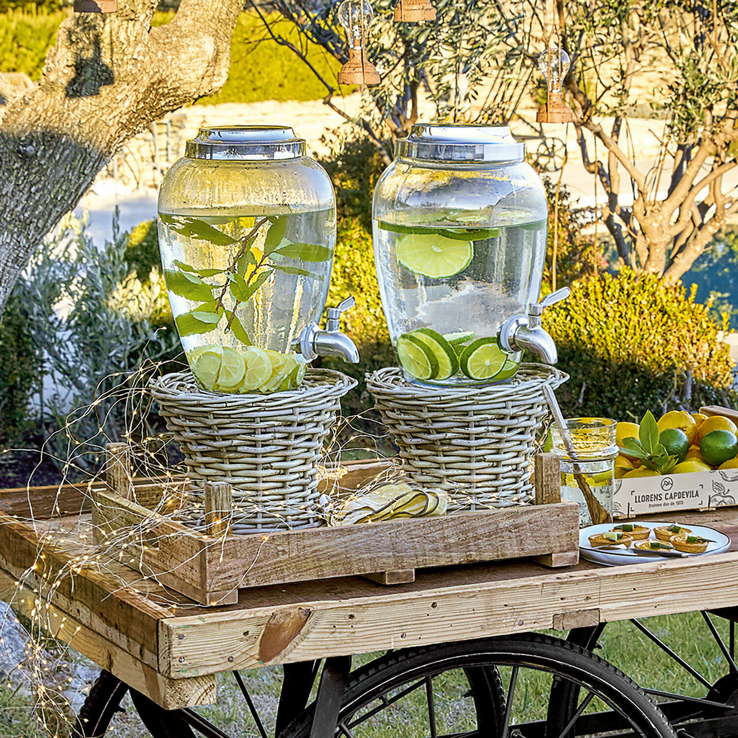 Support Duras Carafes en verre avec robinet sur supports en osier posées sur une charrette en bois dans un jardin
