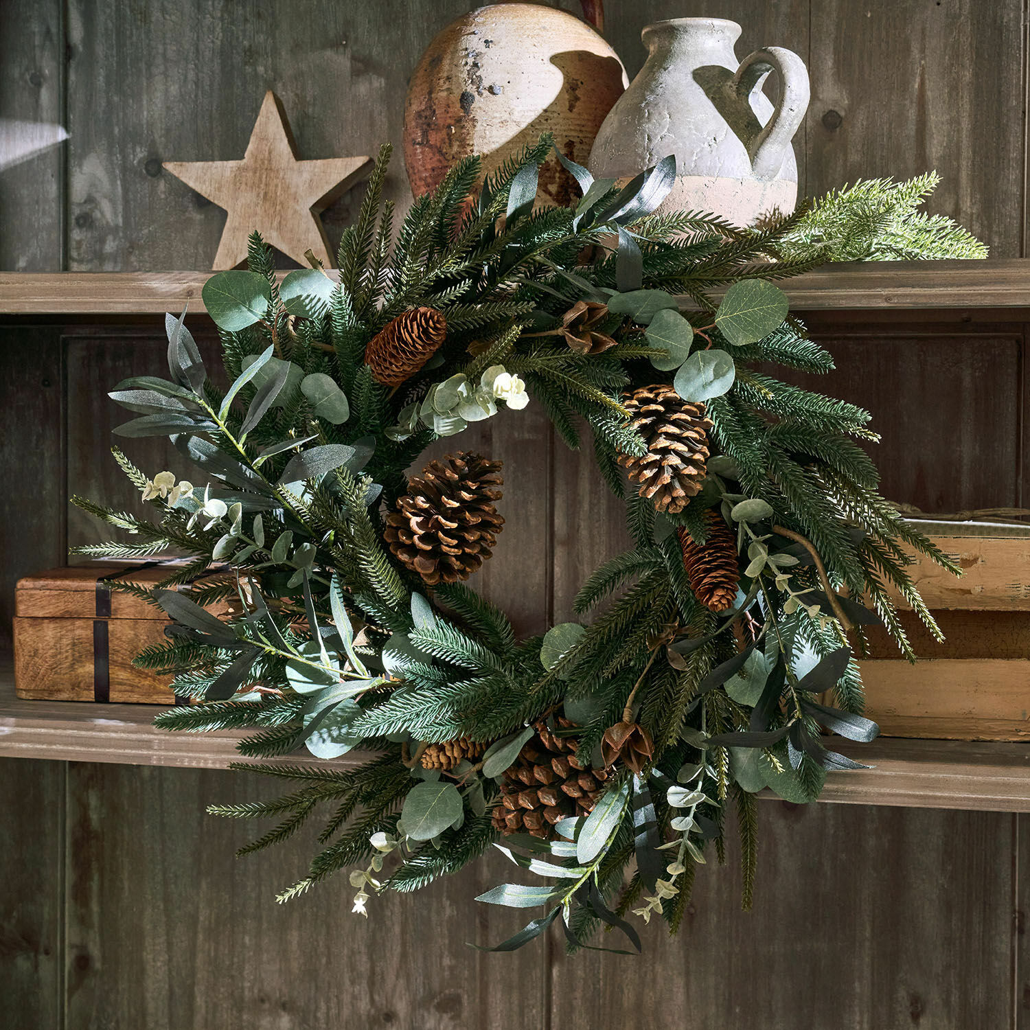 Couronne Rosella Couronne décorative de Noël avec branches vertes et pommes de pin sur étagère en bois rustique
