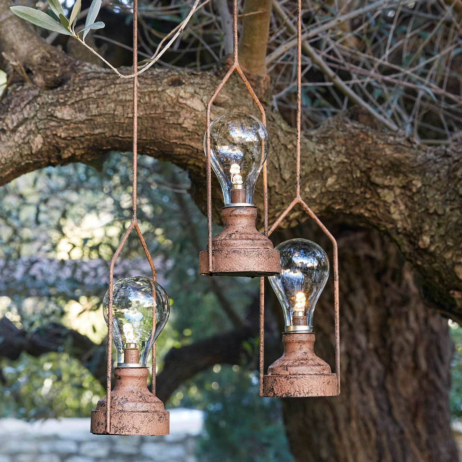 Trois lampes suspendues en métal rouillé avec ampoules LED devant un arbre, éclairage décoratif extérieur