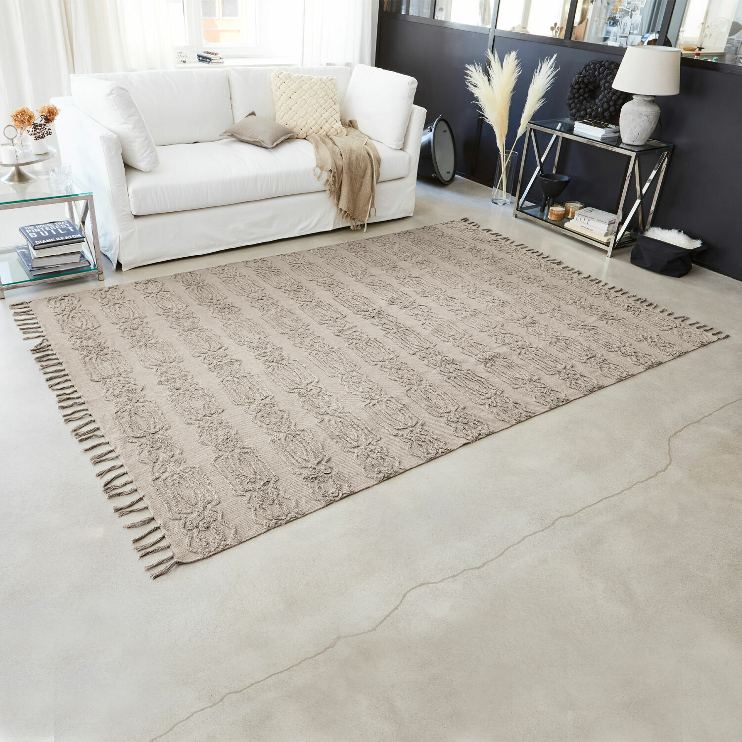 Tapis beige en coton avec franges et motif, dans un salon moderne avec canapé blanc et décorations