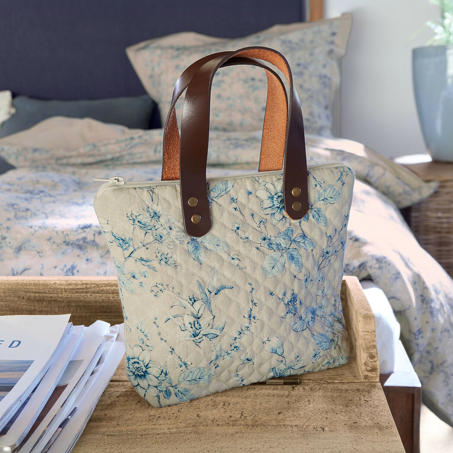 Cabas Vailenne Sac matelassé beige à motif floral bleu avec poignées en cuir marron posé sur une table en bois