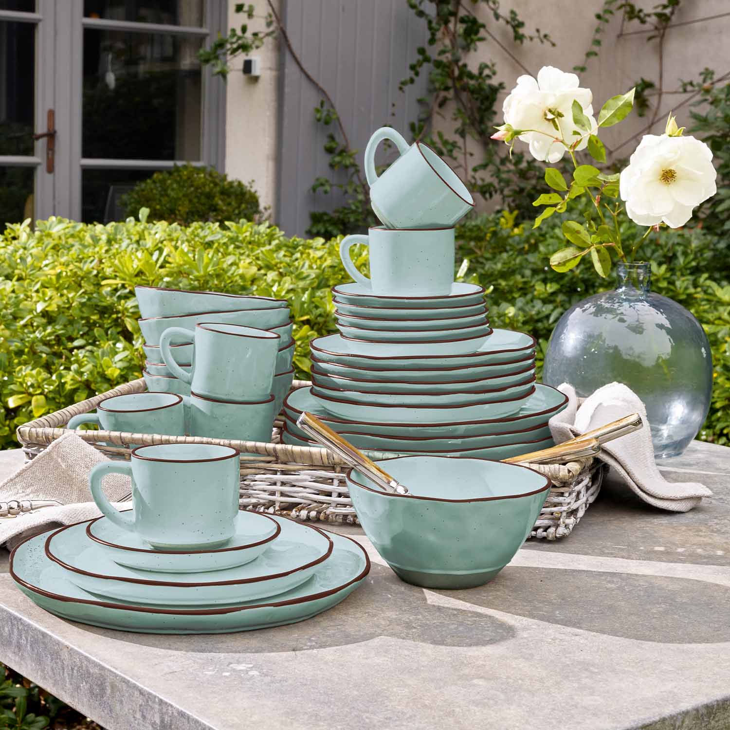 Service de vaisselle en céramique vert menthe avec bordure marron posé sur une table de jardin