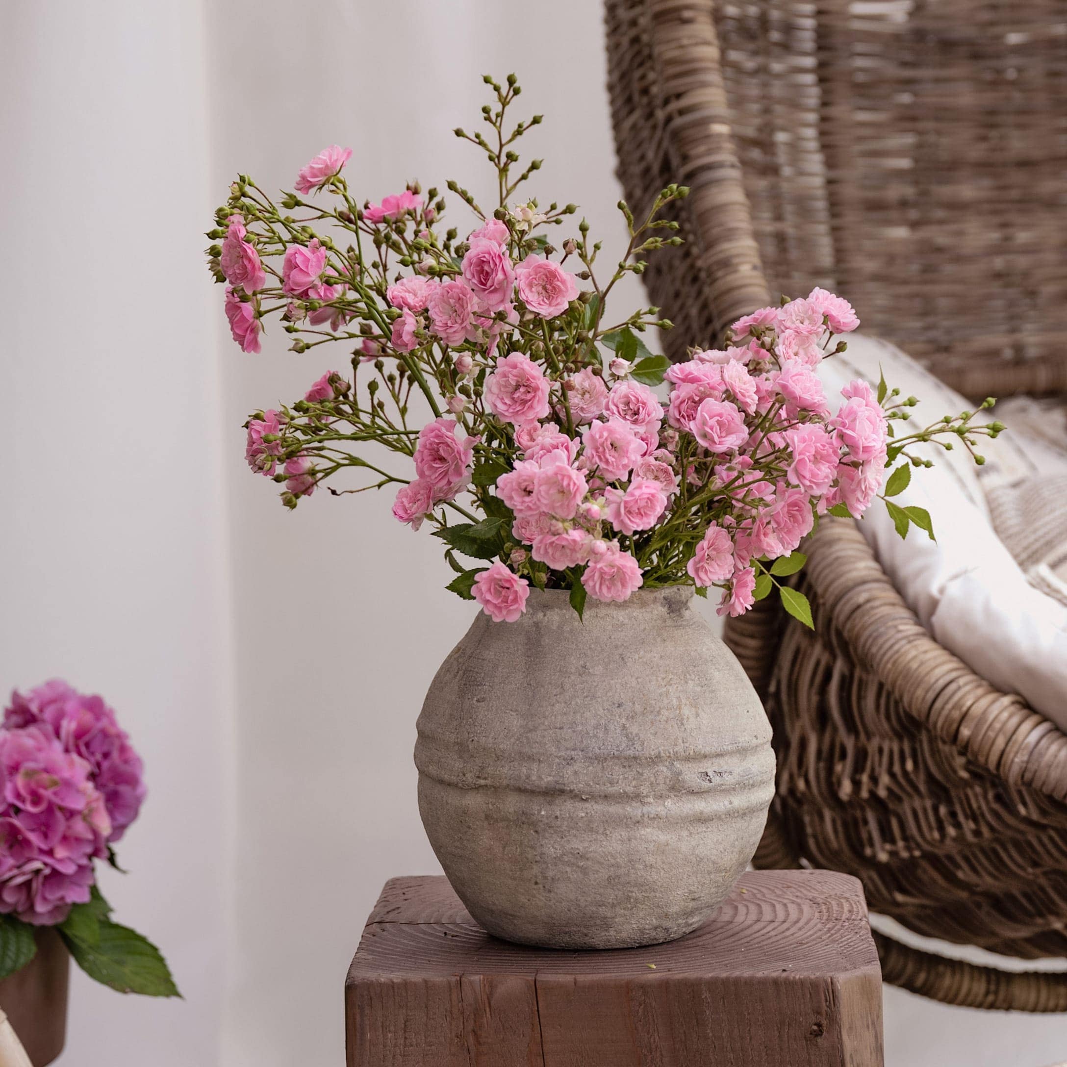 Vase en céramique grise avec fleurs roses sur table en bois dans un intérieur chaleureux