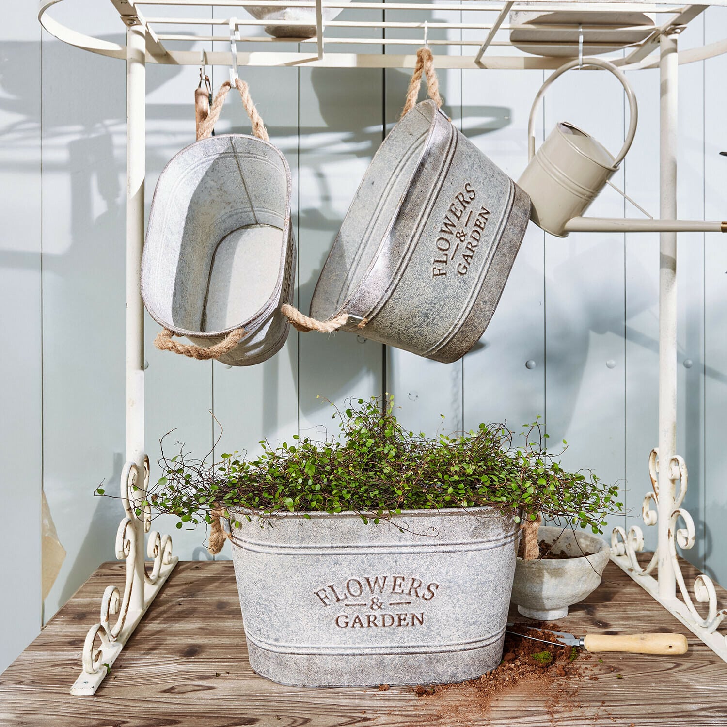 Lot de 3 cache-pots Merrin Pots en métal gris avec inscription Flowers & Garden, plante verte et outil de jardinage sur table en bois