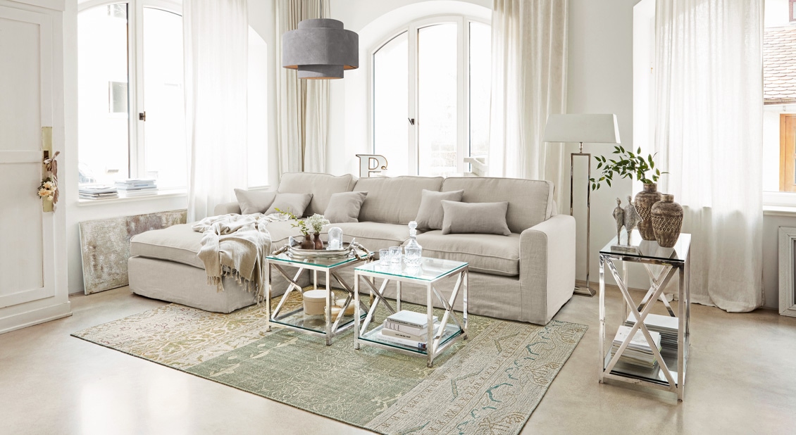 Canapé beige aspect lin avec coussins et tables basses en métal dans un salon lumineux