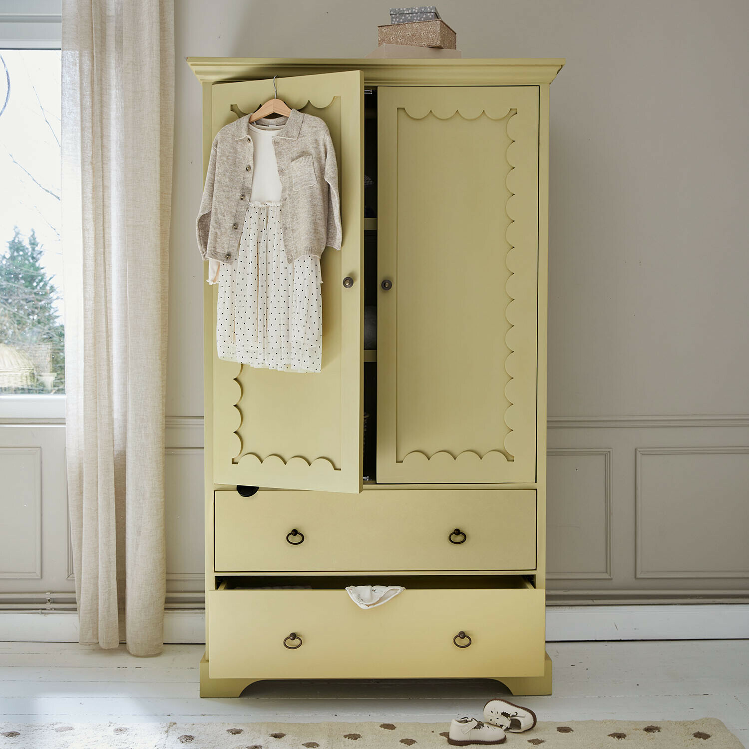 Armoire pour enfant Frollin Armoire en bois jaune avec portes décoratives et vêtements d'enfant suspendus dans une pièce lumineuse