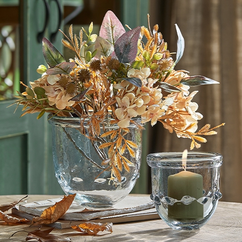 Vase en verre avec fleurs séchées beige et marron et photophore avec bougie sur table en bois