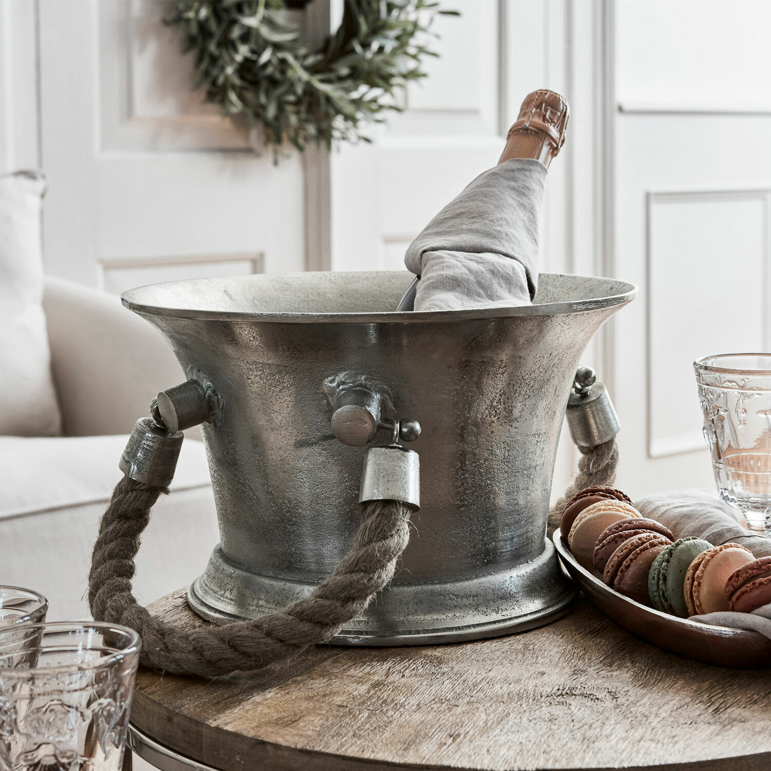 Seau à champagne Maxwell Seau à glace en métal avec poignée en corde épaisse et bouteille de champagne enveloppée de tissu gris sur table en bois
