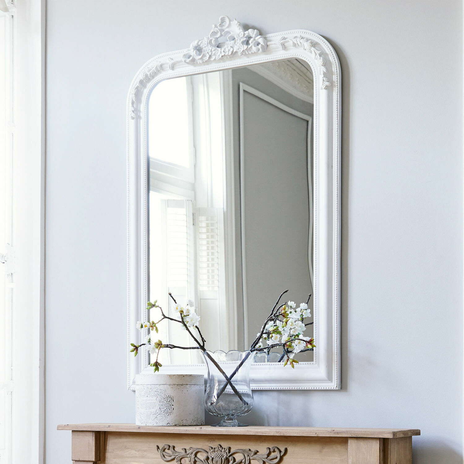 Miroir Aubais Miroir décoratif blanc avec cadre en résine au-dessus d'une cheminée en bois avec vase et fleurs