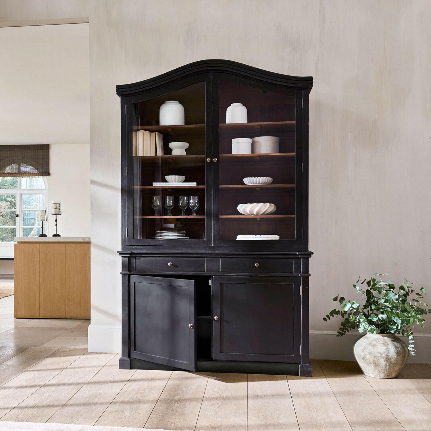 Vitrine Westridge Vitrine en bois noir avec portes vitrées et étagères décorées de céramiques blanches et verres dans un salon
