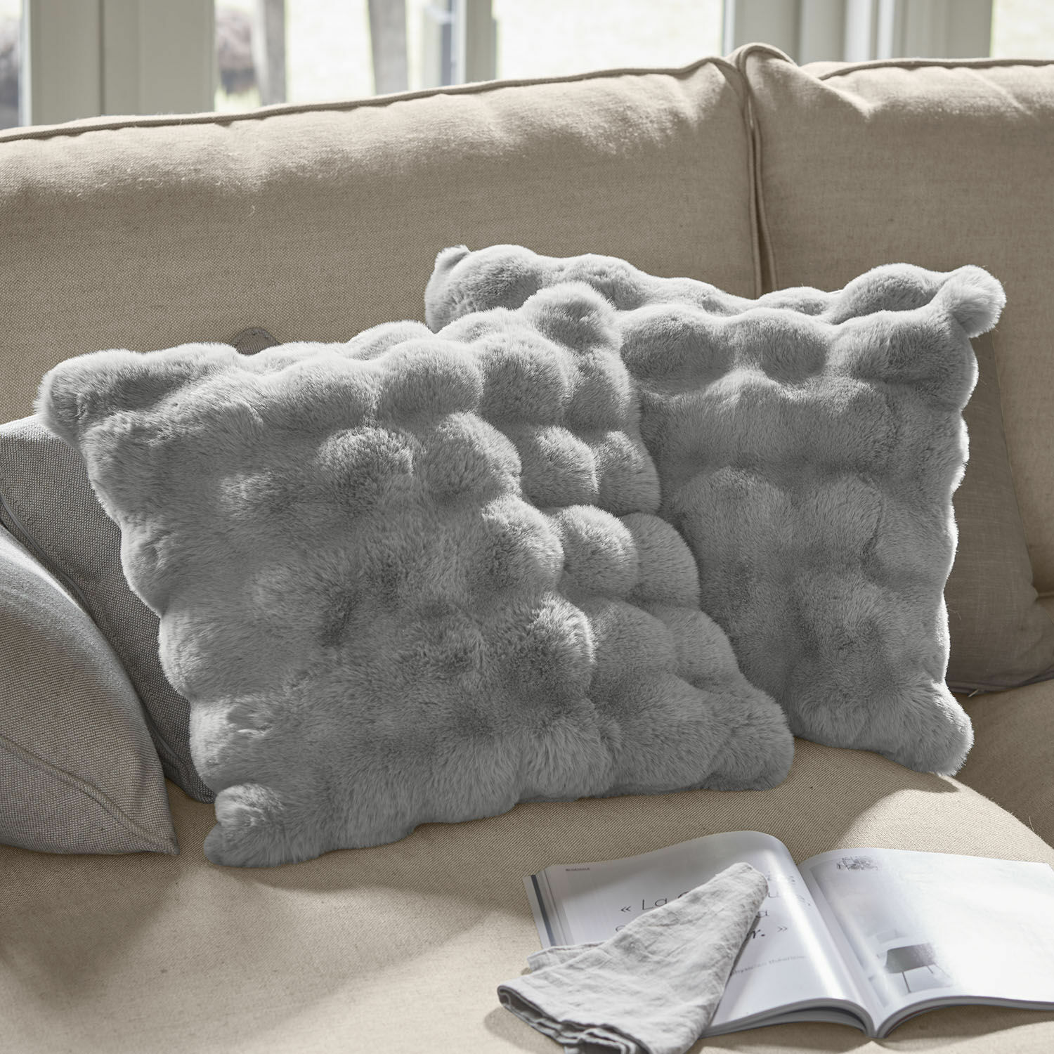 Lot de 2 housses de coussins Zalina Coussins décoratifs gris en fausse fourrure sur canapé beige, parfaits pour salon confortable