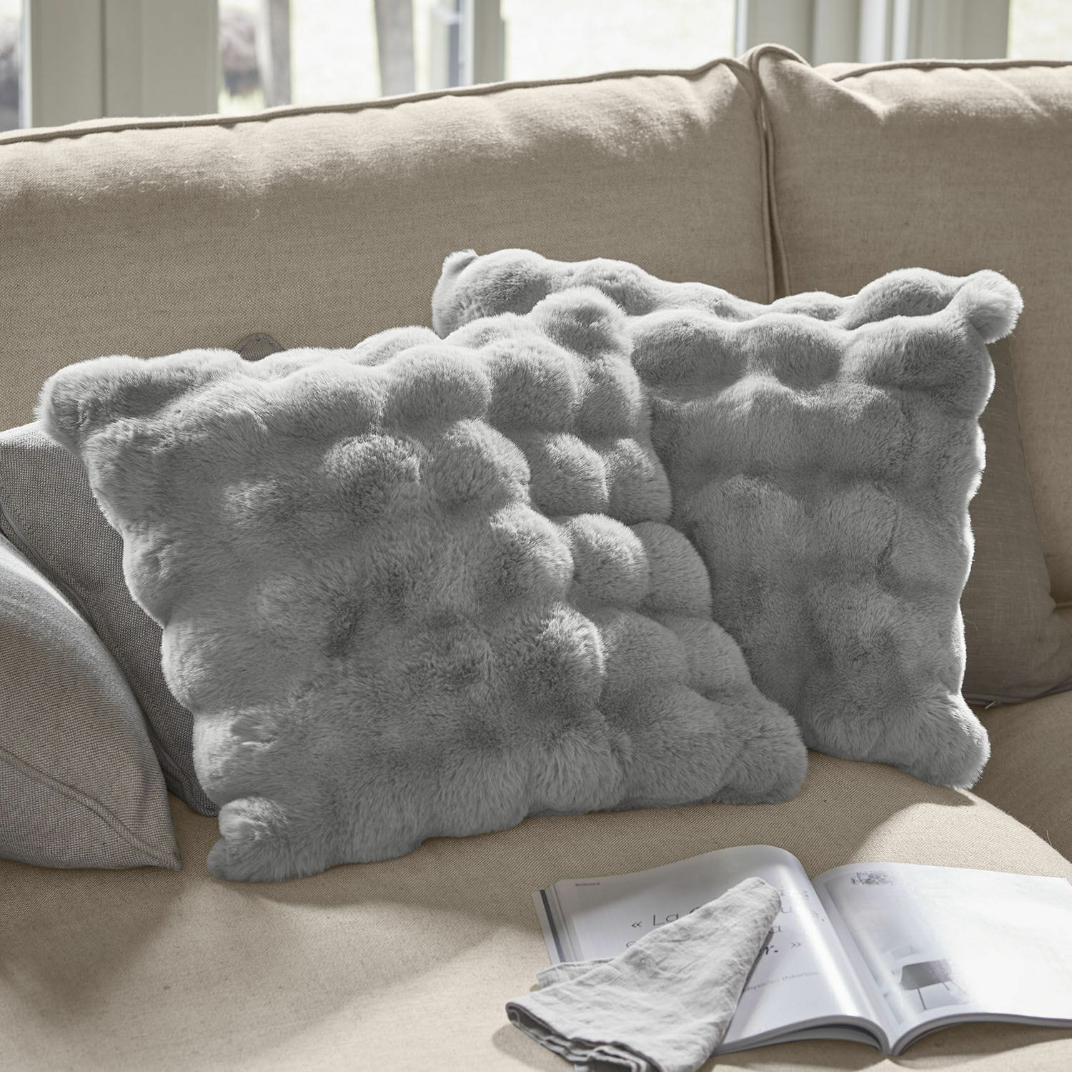 Lot de 2 housses de coussins Zalina Coussins décoratifs gris en fausse fourrure sur canapé beige, parfaits pour salon confortable