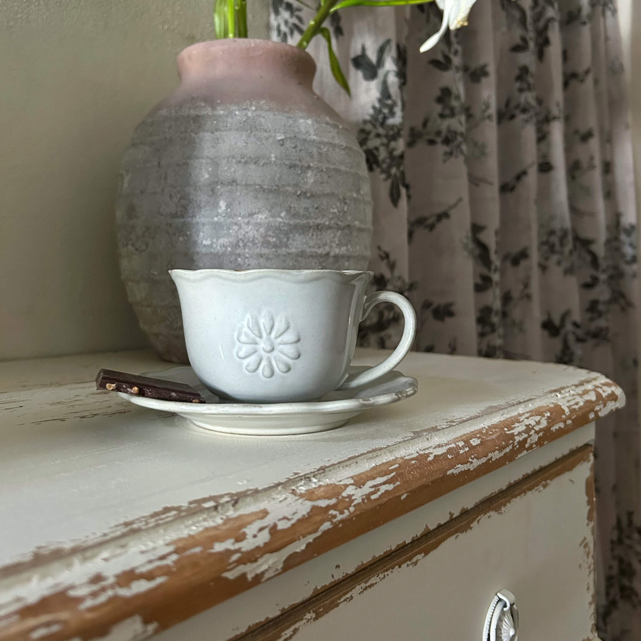 Tasse en céramique blanche avec soucoupe et morceau de chocolat sur un meuble en bois vieilli