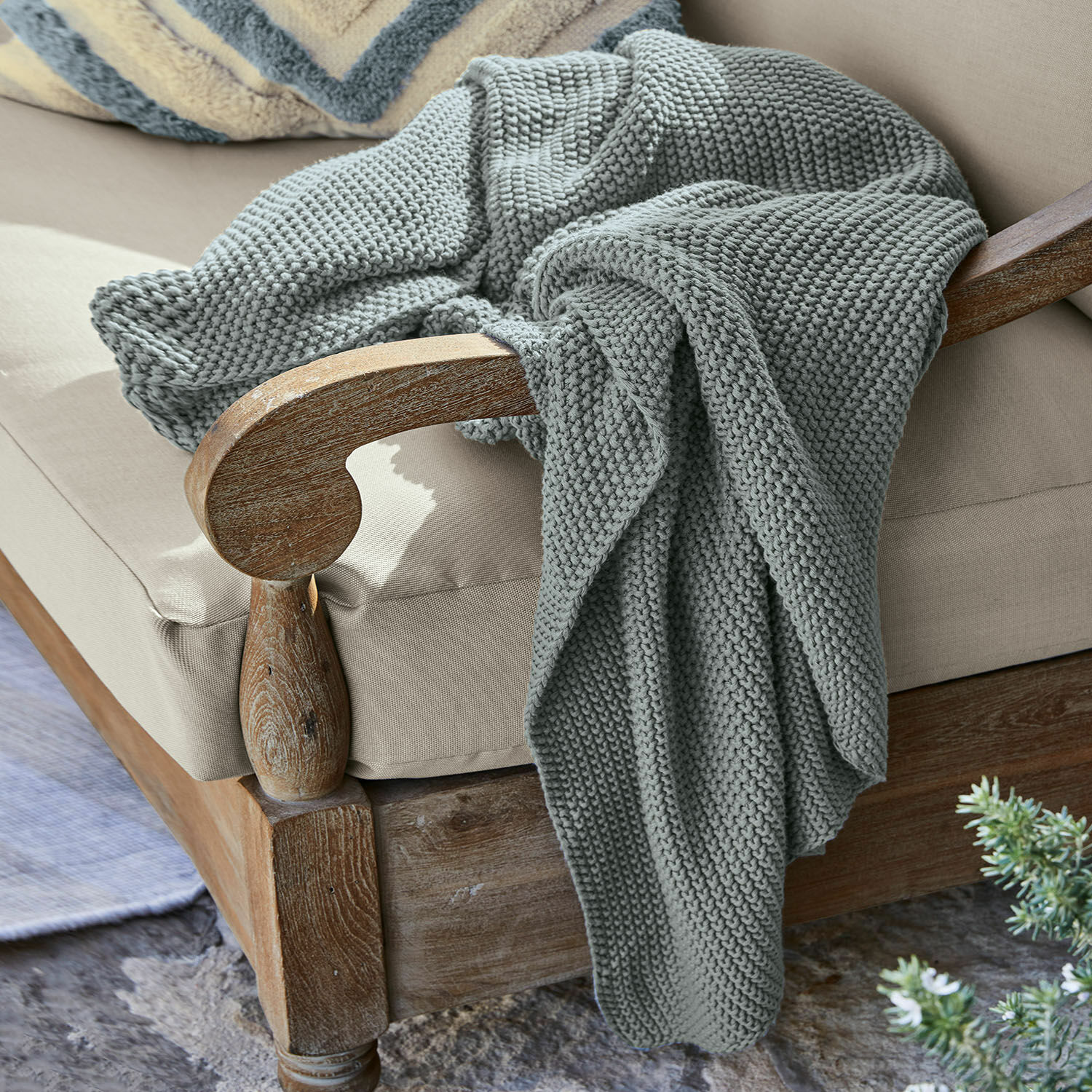 Plaid Ancy Plaid gris épais en maille douce posé sur un fauteuil en bois avec coussin beige