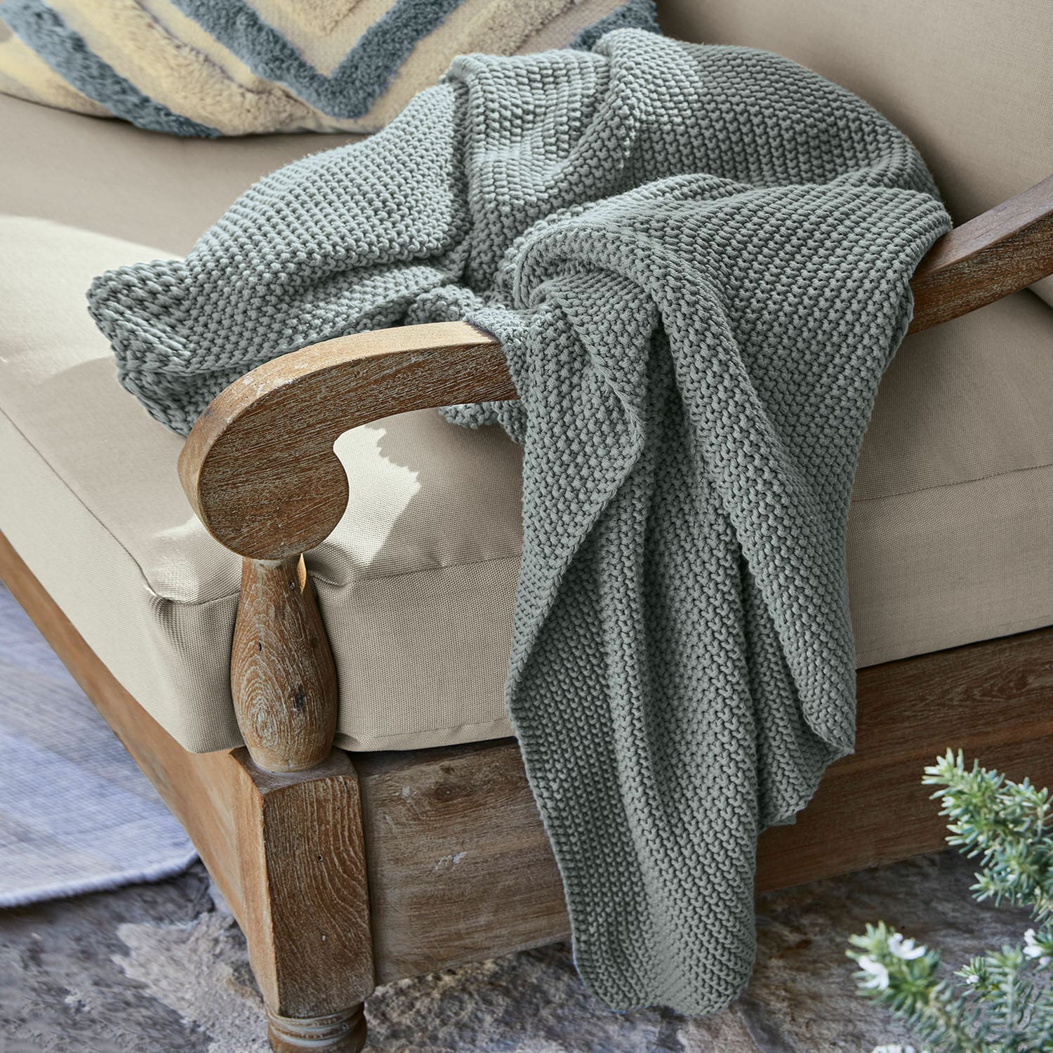 Plaid Ancy Plaid gris épais en maille douce posé sur un fauteuil en bois avec coussin beige
