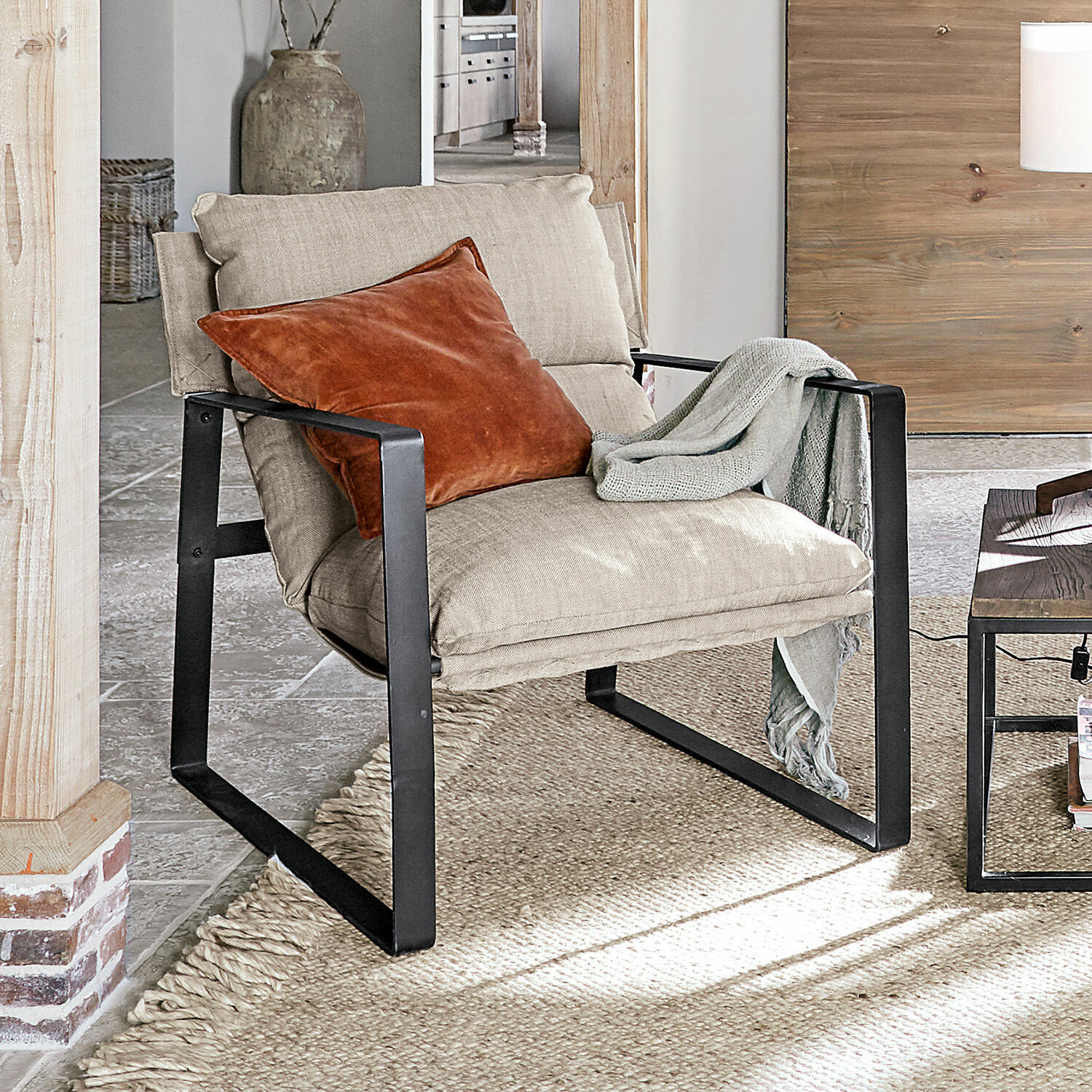 Fauteuil Seuvard Fauteuil en tissu beige avec cadre métallique noir, coussin orange et plaid gris dans un salon lumineux