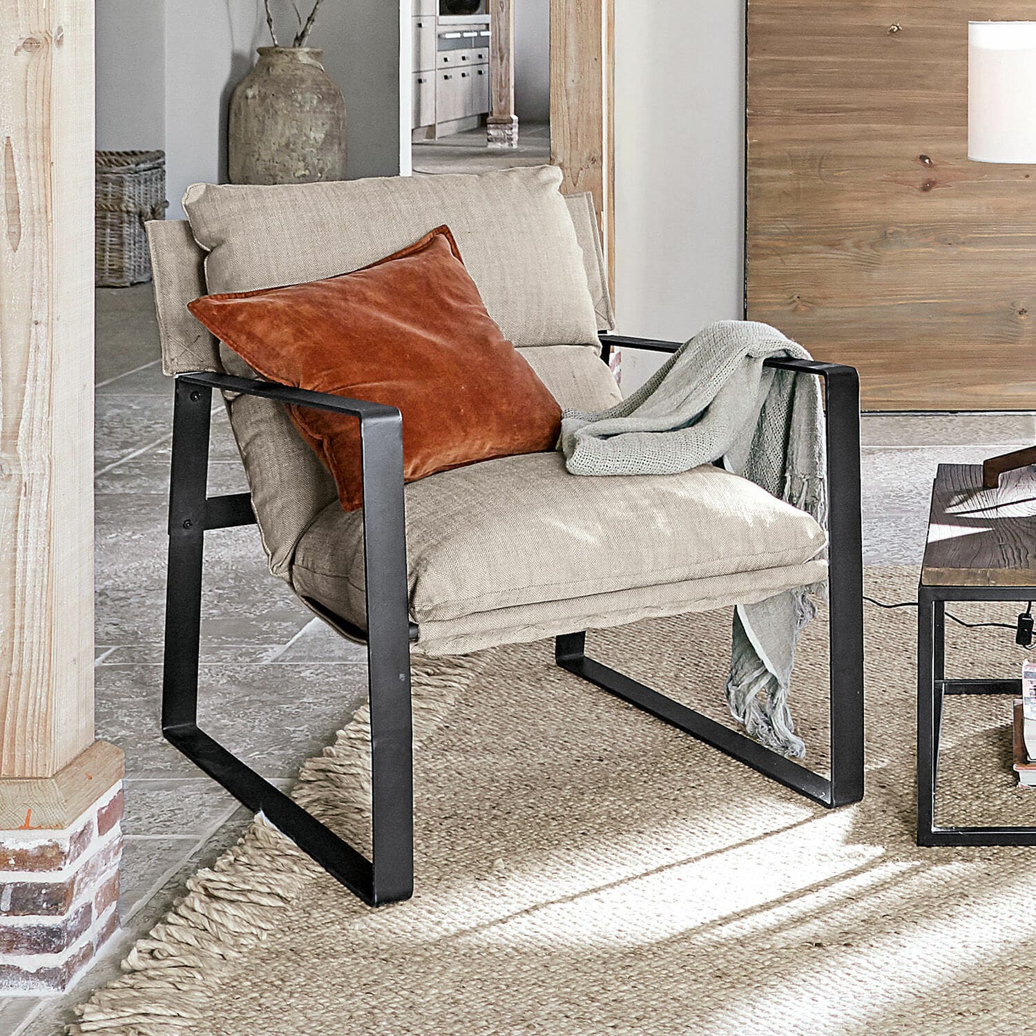 Fauteuil Seuvard Fauteuil en tissu beige avec cadre métallique noir, coussin orange et plaid gris dans un salon lumineux