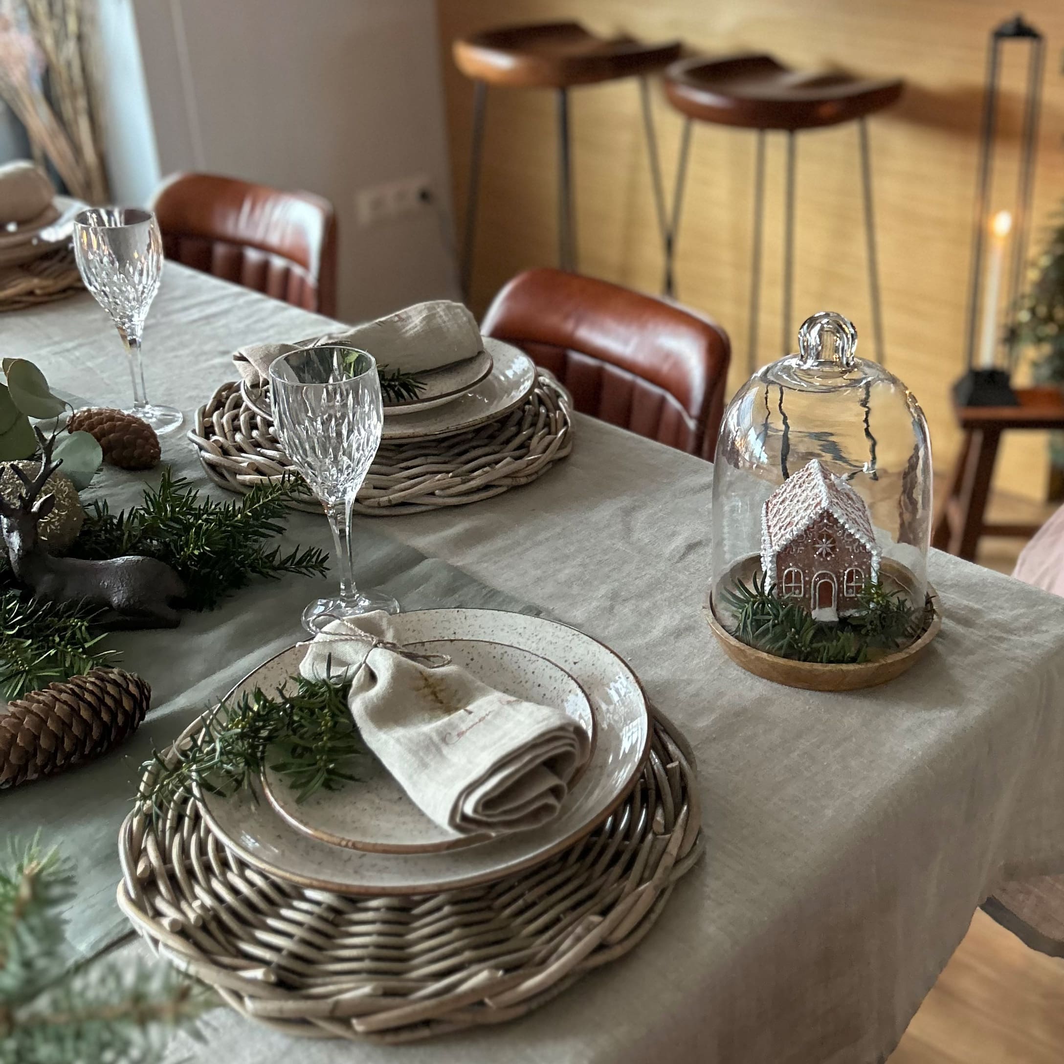 Table élégamment dressée avec sets en osier, assiettes en céramique et décoration de Noël sous cloche en verre