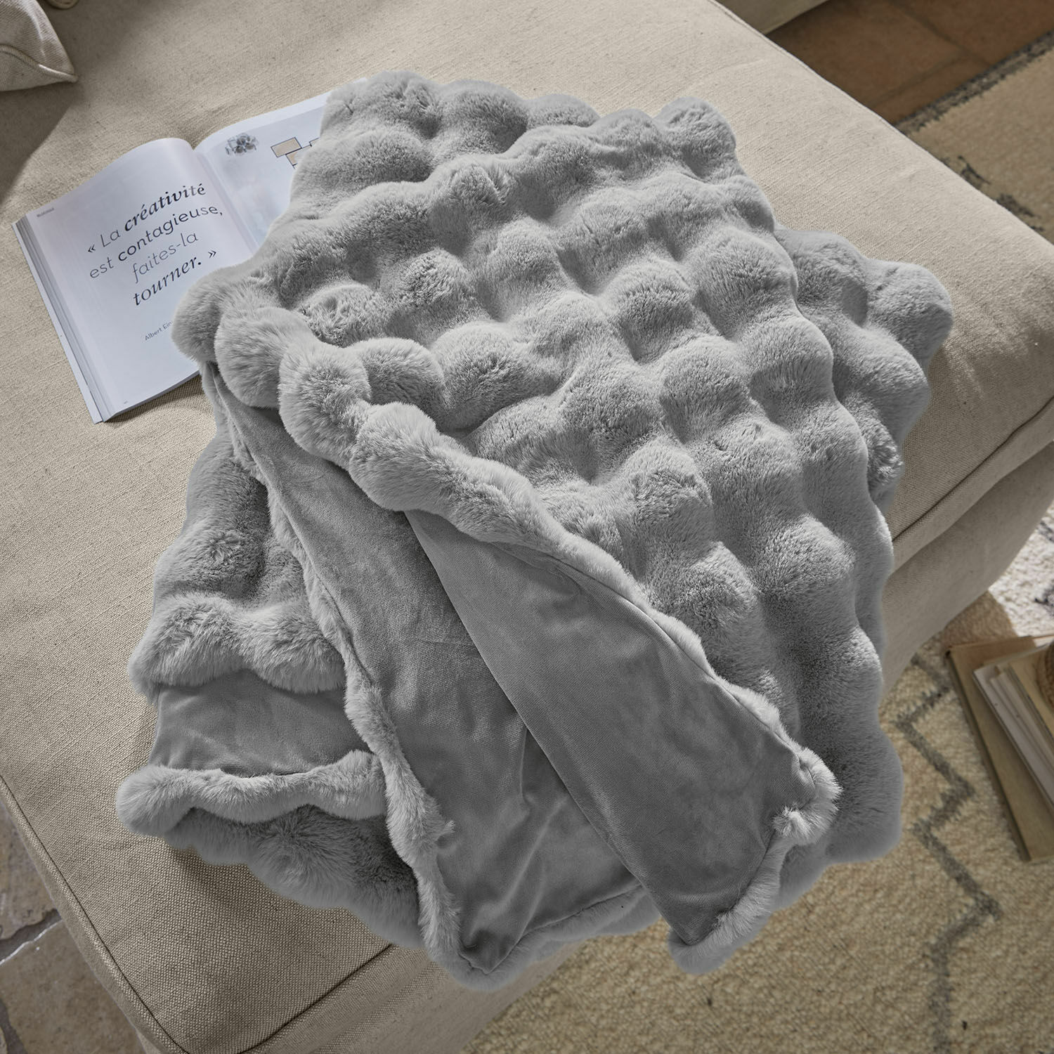 Plaid Zalina Plaid gris doux en fausse fourrure sur un canapé beige, parfait pour la décoration et la chaleur intérieure