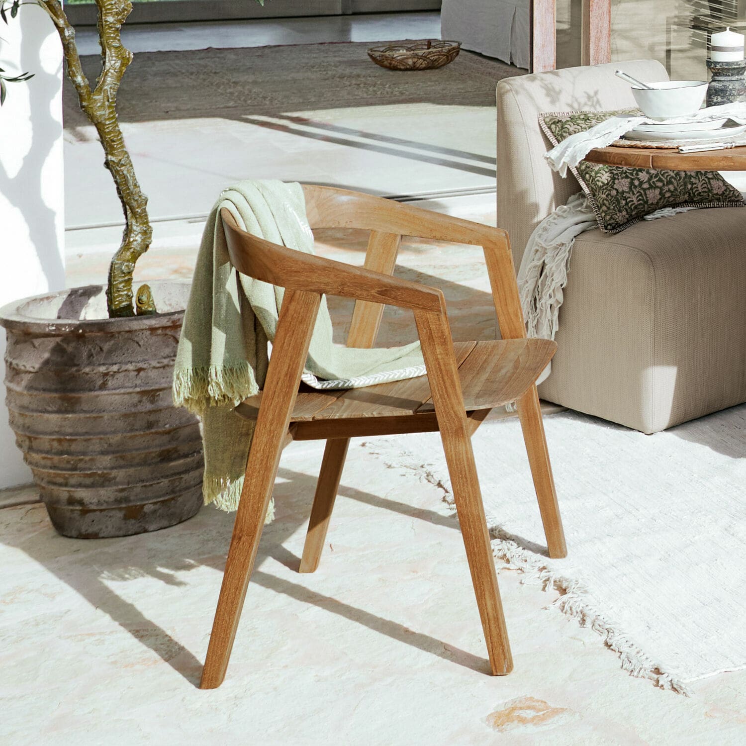Chaise Saulny Chaise en bois naturel avec accoudoirs et plaid vert posée sur une terrasse lumineuse