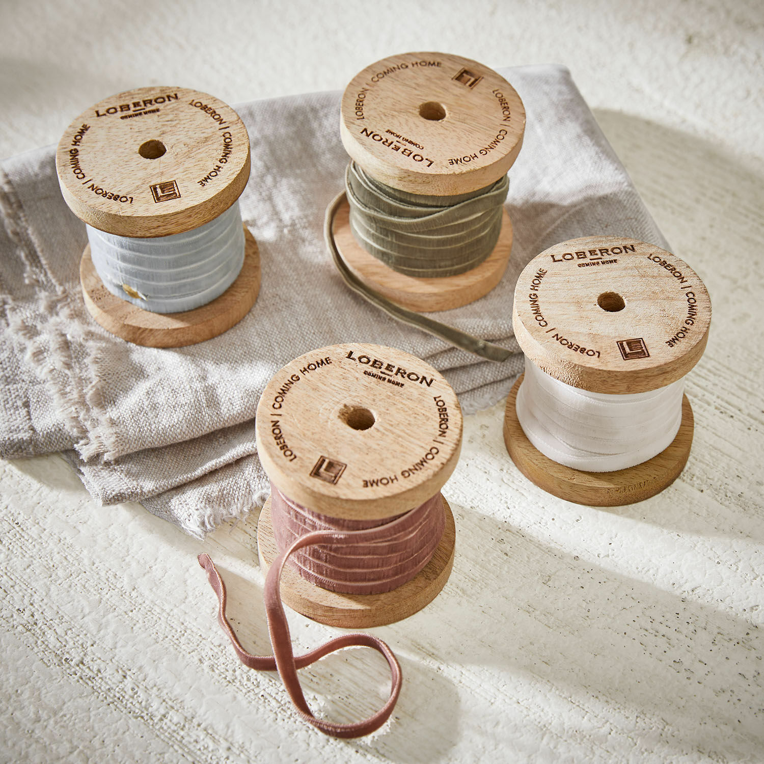 Lot de 4 rubans de velours Hilary Bobines en bois avec rubans en velours pastel posées sur tissu en lin, décoration intérieure élégante