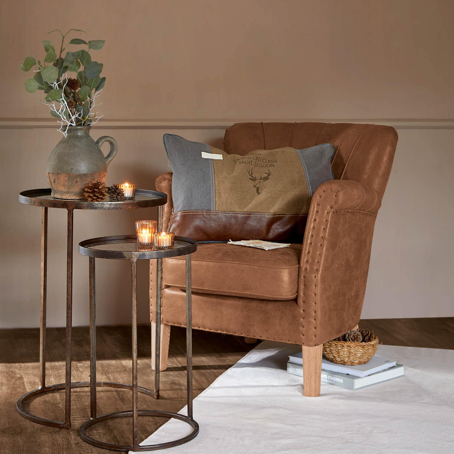 Fauteuil marron en simili cuir avec coussin décoratif et tables métalliques avec bougies et vase