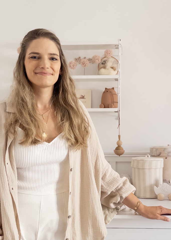 Femme en chemise beige et haut blanc dans une pièce claire avec décorations pour enfants