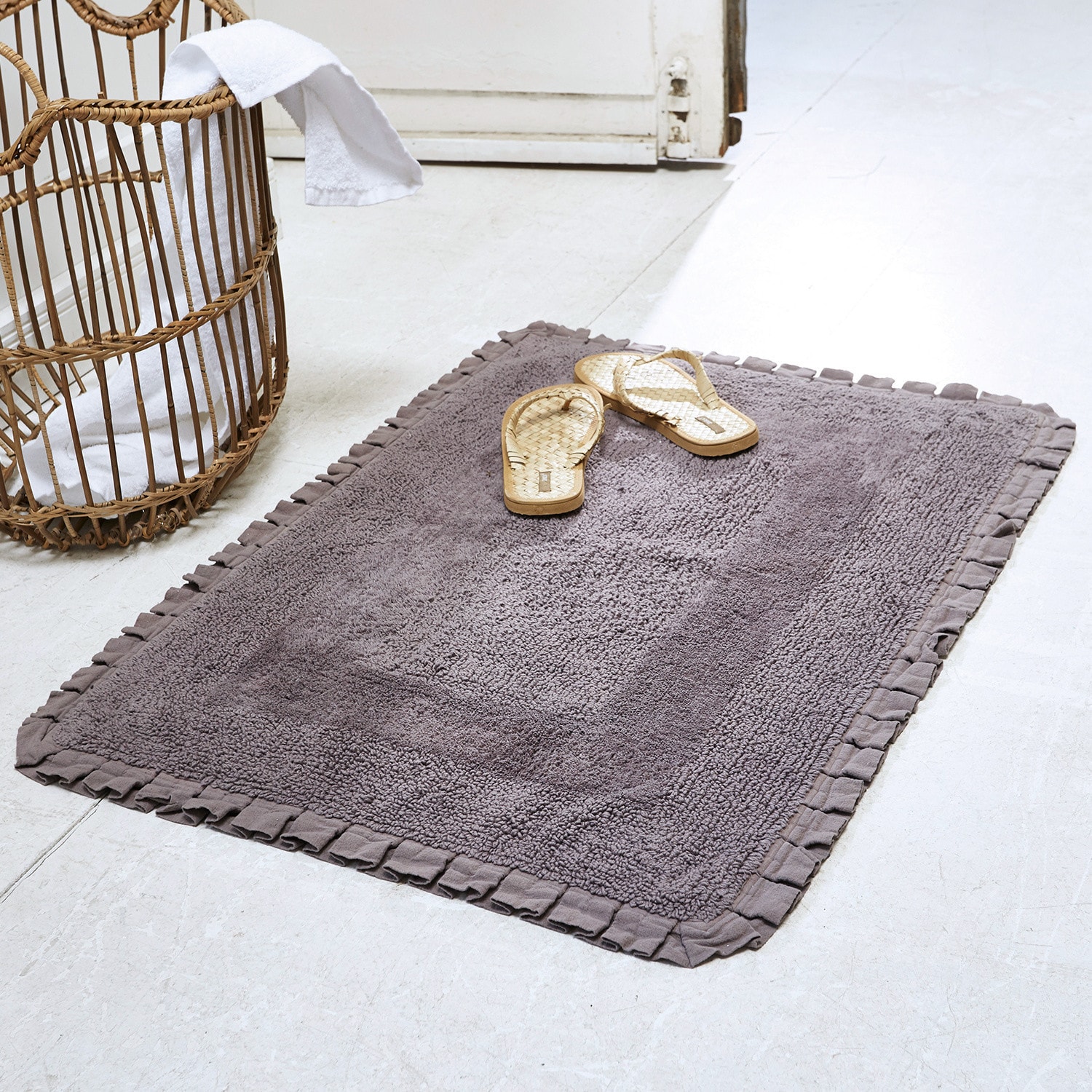 Tapis de bain Jasmin Tapis de bain gris en coton avec bordure plissée sur sol clair avec sandales en rotin