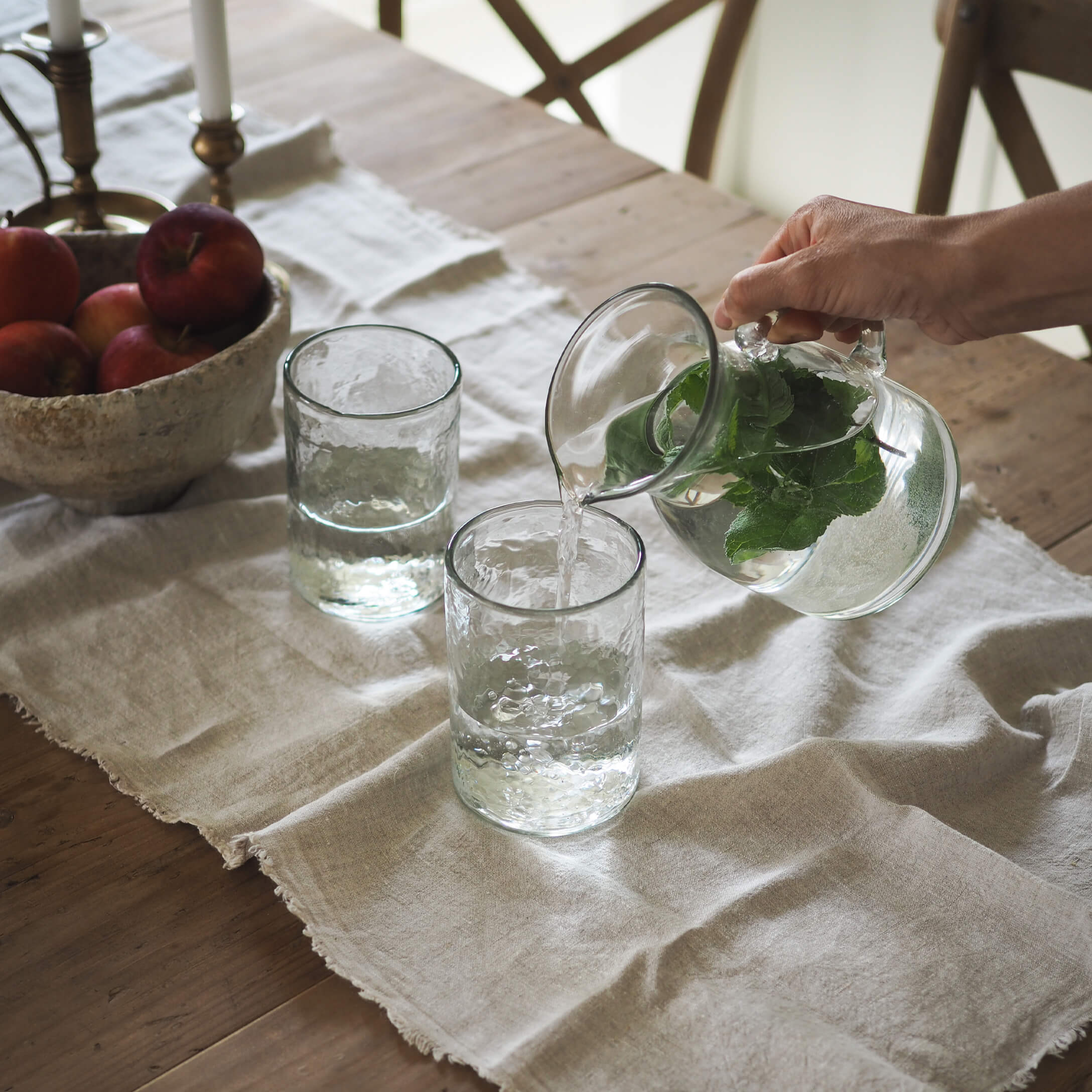 Carafe en verre avec feuilles vertes et deux verres sur une nappe en lin sur une table en bois