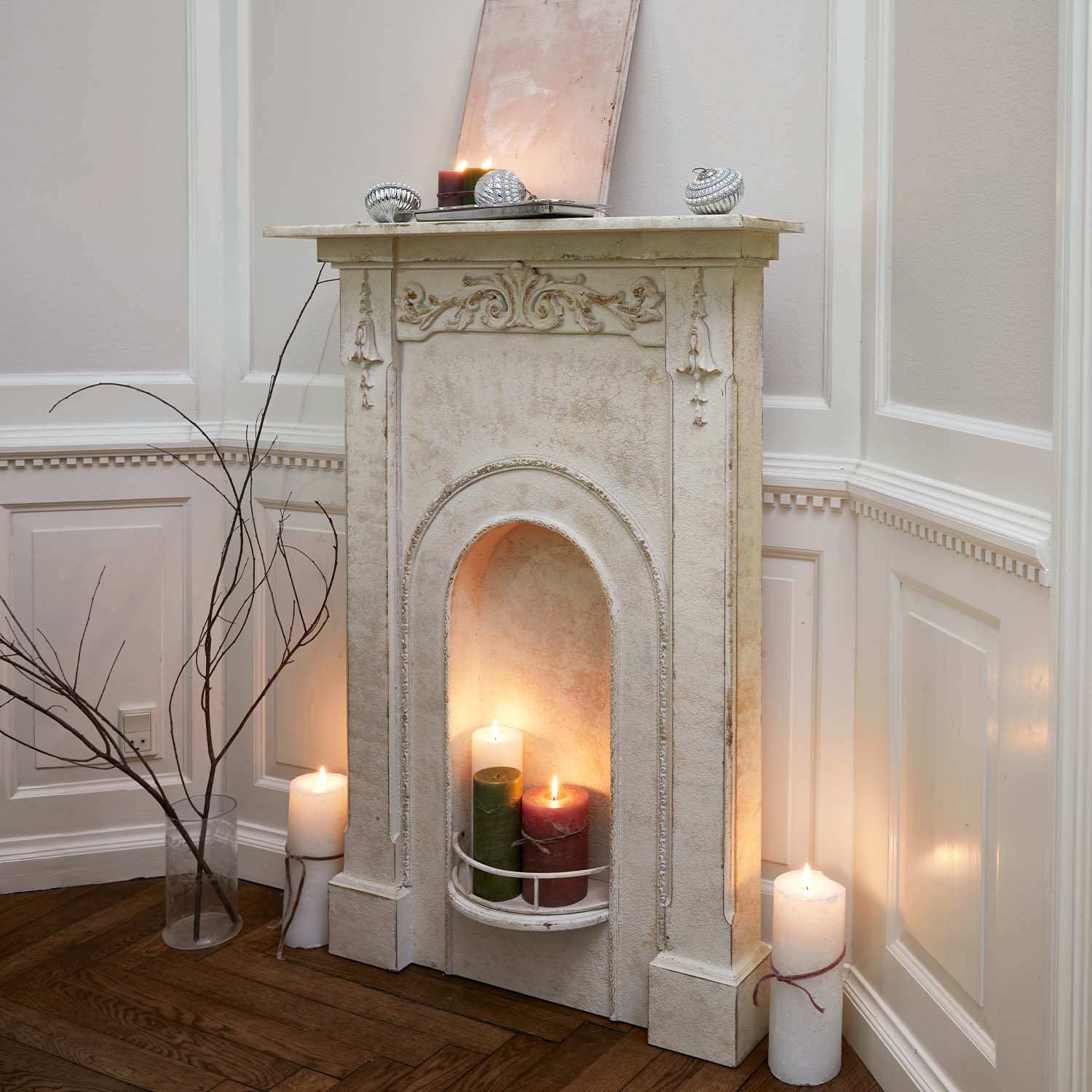 Cheminée décorative blanche avec reliefs sculptés et bougies allumées dans un intérieur rustique