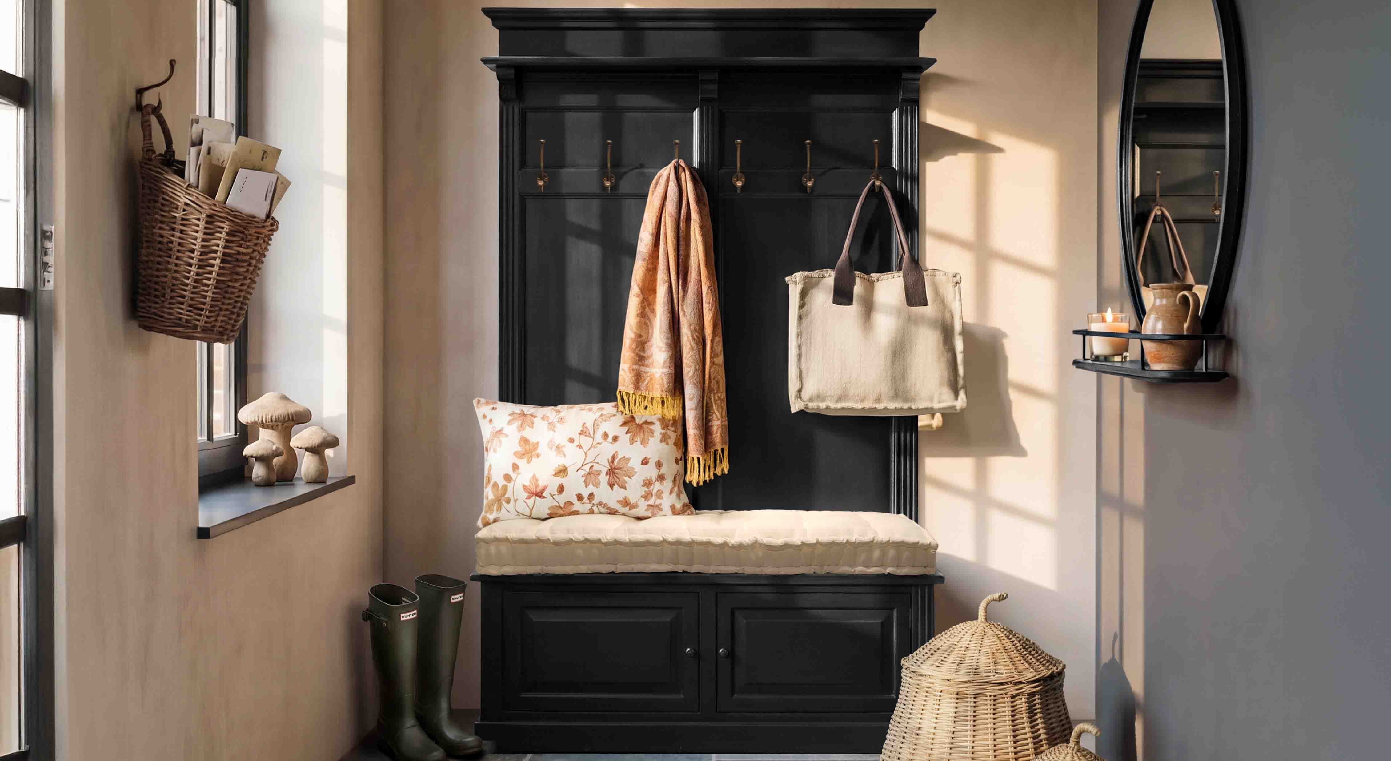 Meuble d'entrée noir en bois avec assise rembourrée, coussin et patères dans un couloir chaleureux
