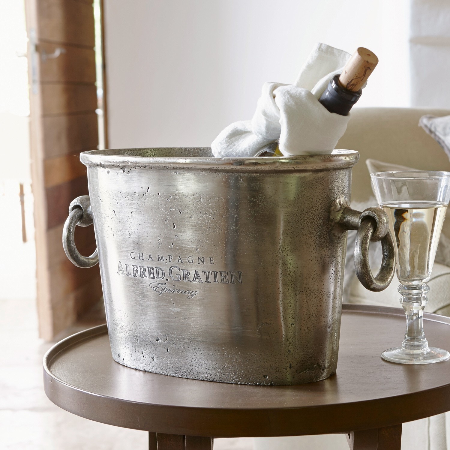 Seau à champagne Alfred Seau à champagne en métal argenté avec poignées et bouteille à l'intérieur sur une table ronde