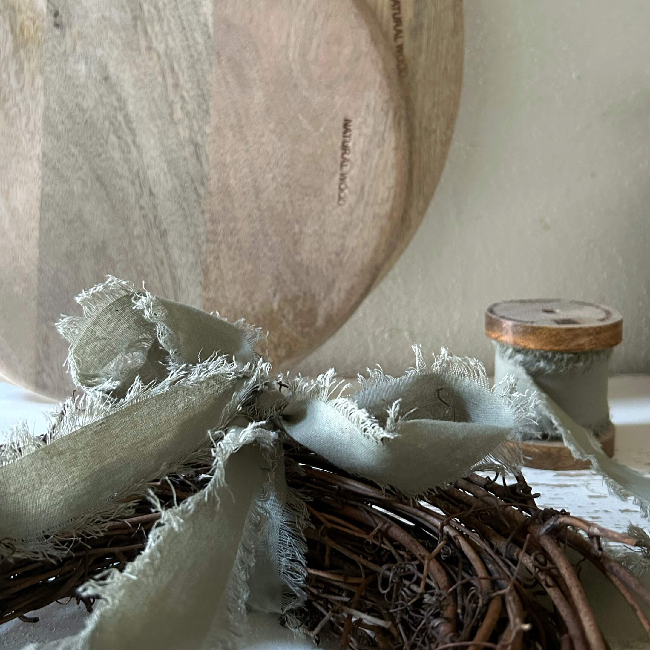 Assiette en bois naturel avec ruban en lin gris sur une couronne en osier pour décoration intérieure