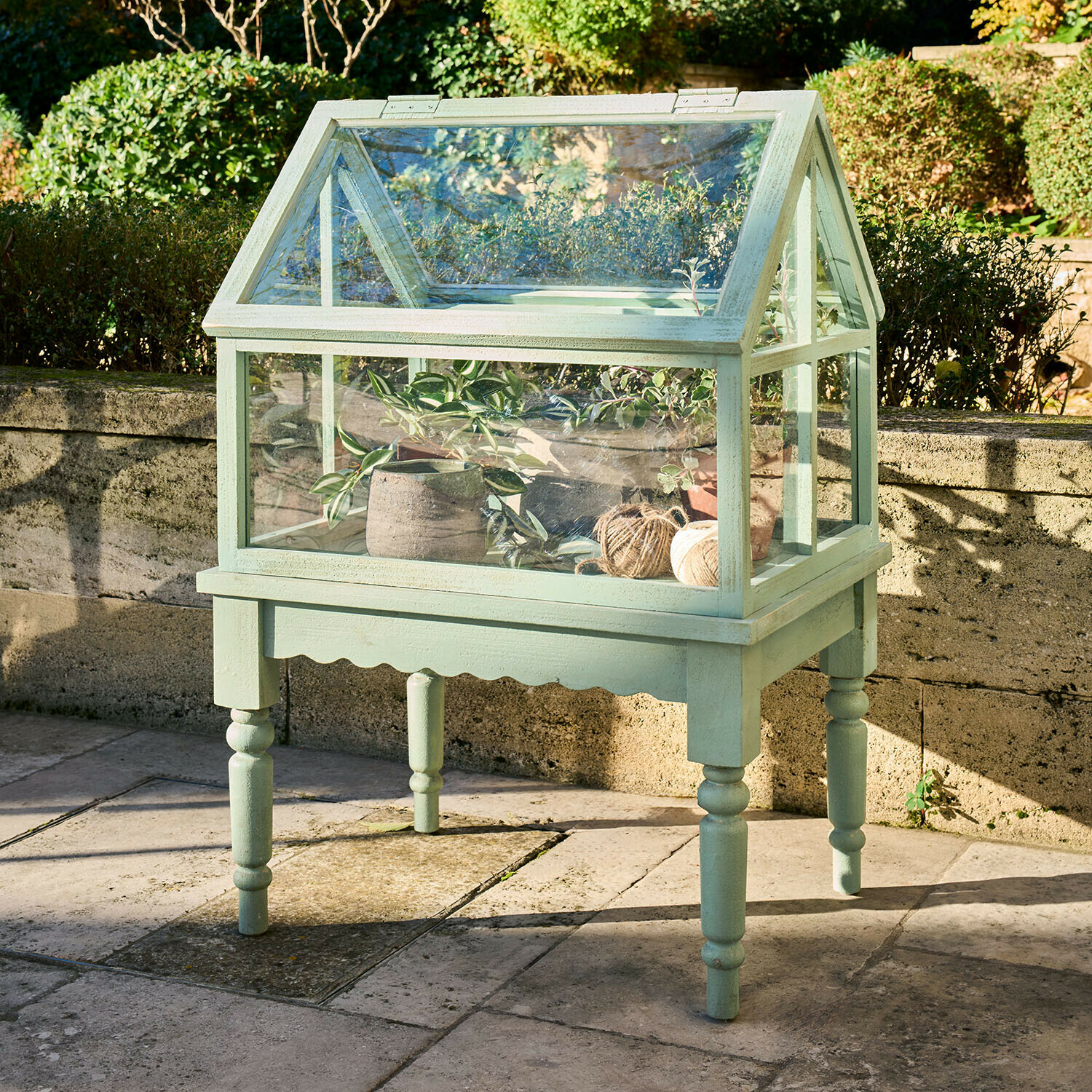 Petite serre verte en bois sur pieds avec plantes et bobines de ficelle pour jardinage