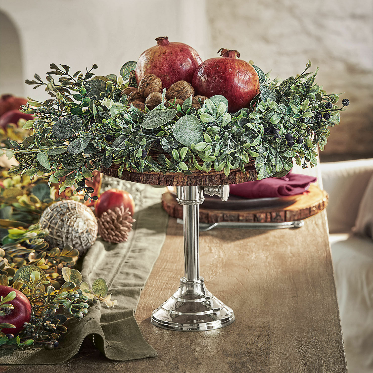 Présentoir Danice II Plateau décoratif en bois et métal avec grenades, noix et feuillage vert sur table en bois