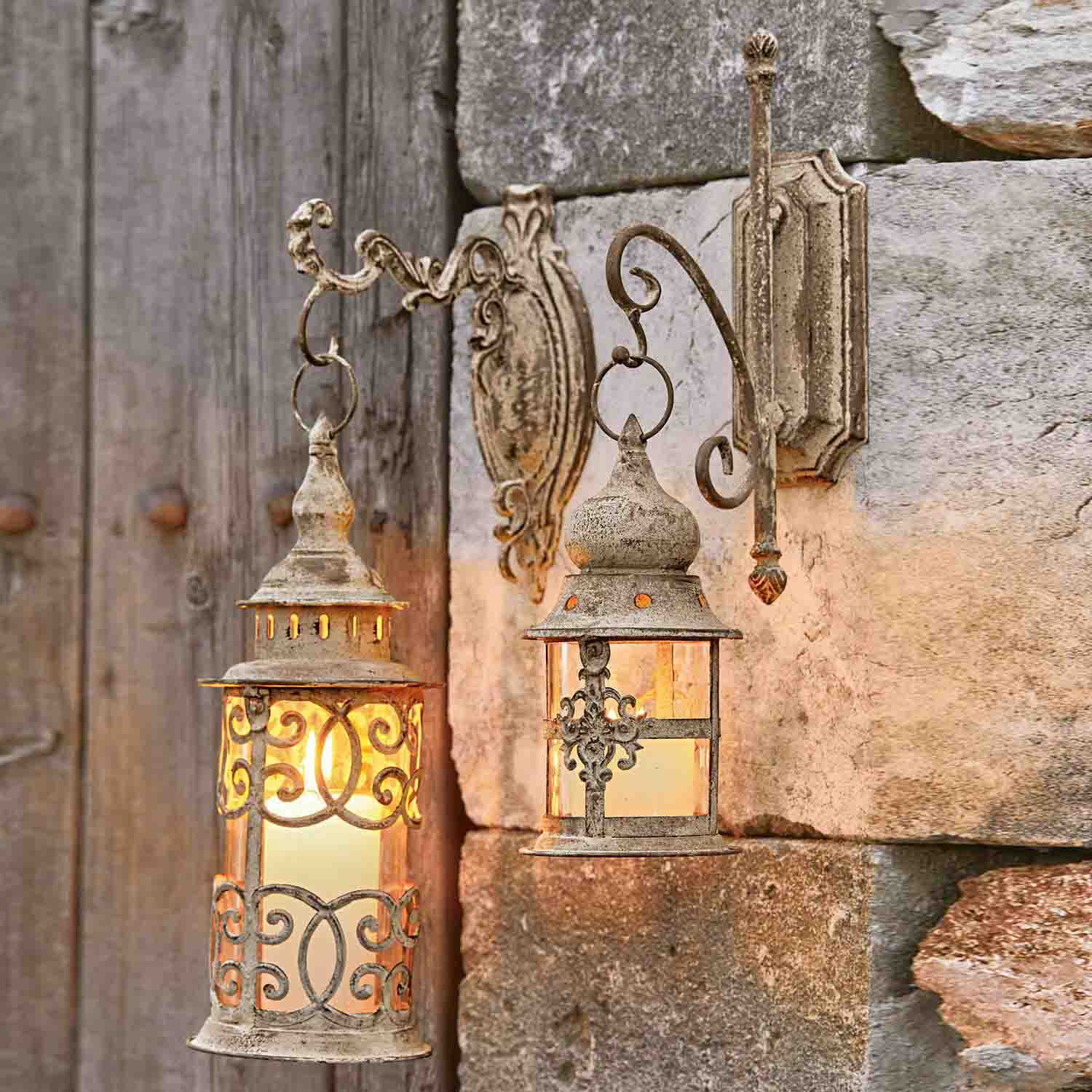 Deux lanternes murales rustiques en métal beige vieilli éclairant un mur en pierre, style vintage