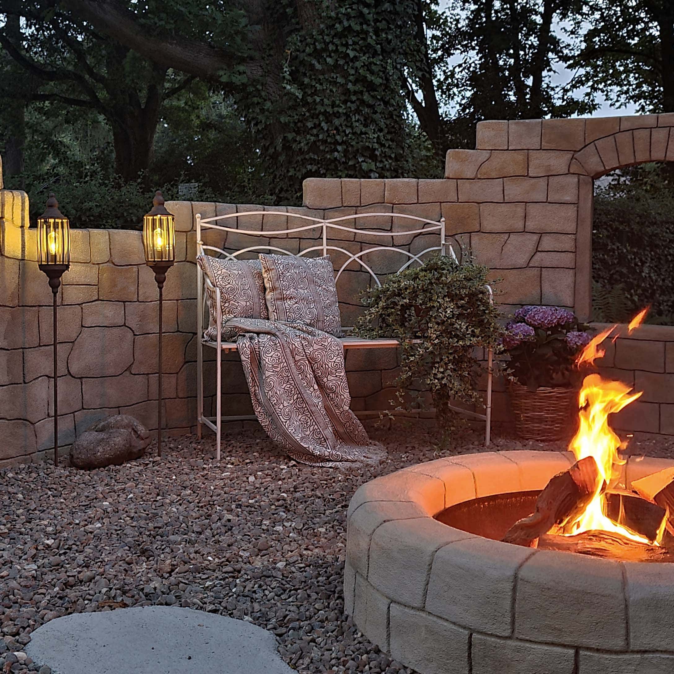 Jardin avec foyer en pierre, banc en métal blanc et lampes sur gravier pour ambiance extérieure