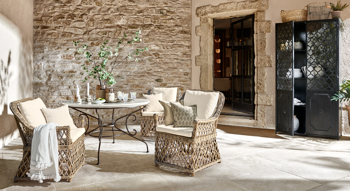Ensemble de meubles de jardin en rotin naturel avec coussins crème et table en métal sur terrasse en pierre