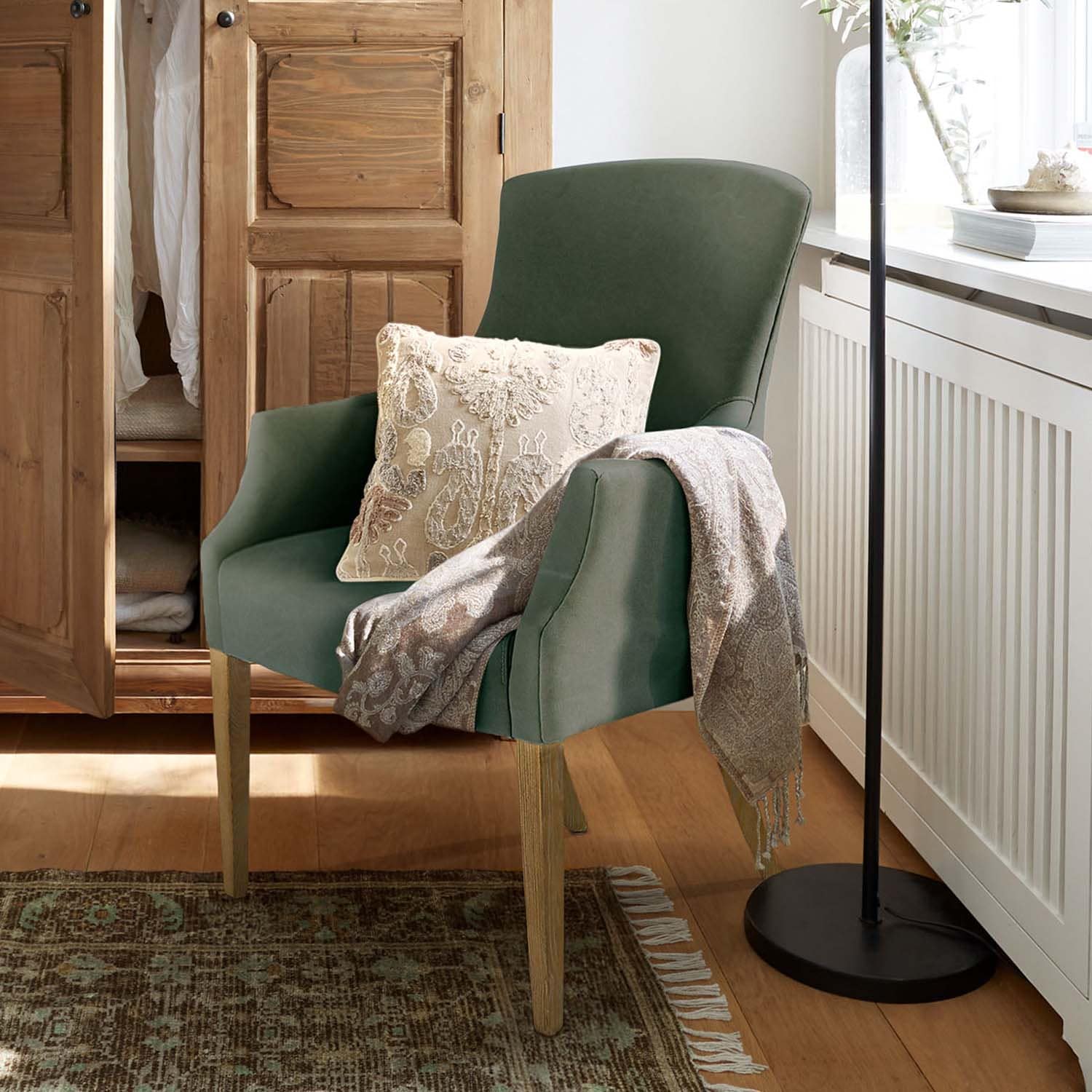 Fauteuil vert en tissu avec pieds en bois, coussin décoratif et plaid gris dans un intérieur chaleureux