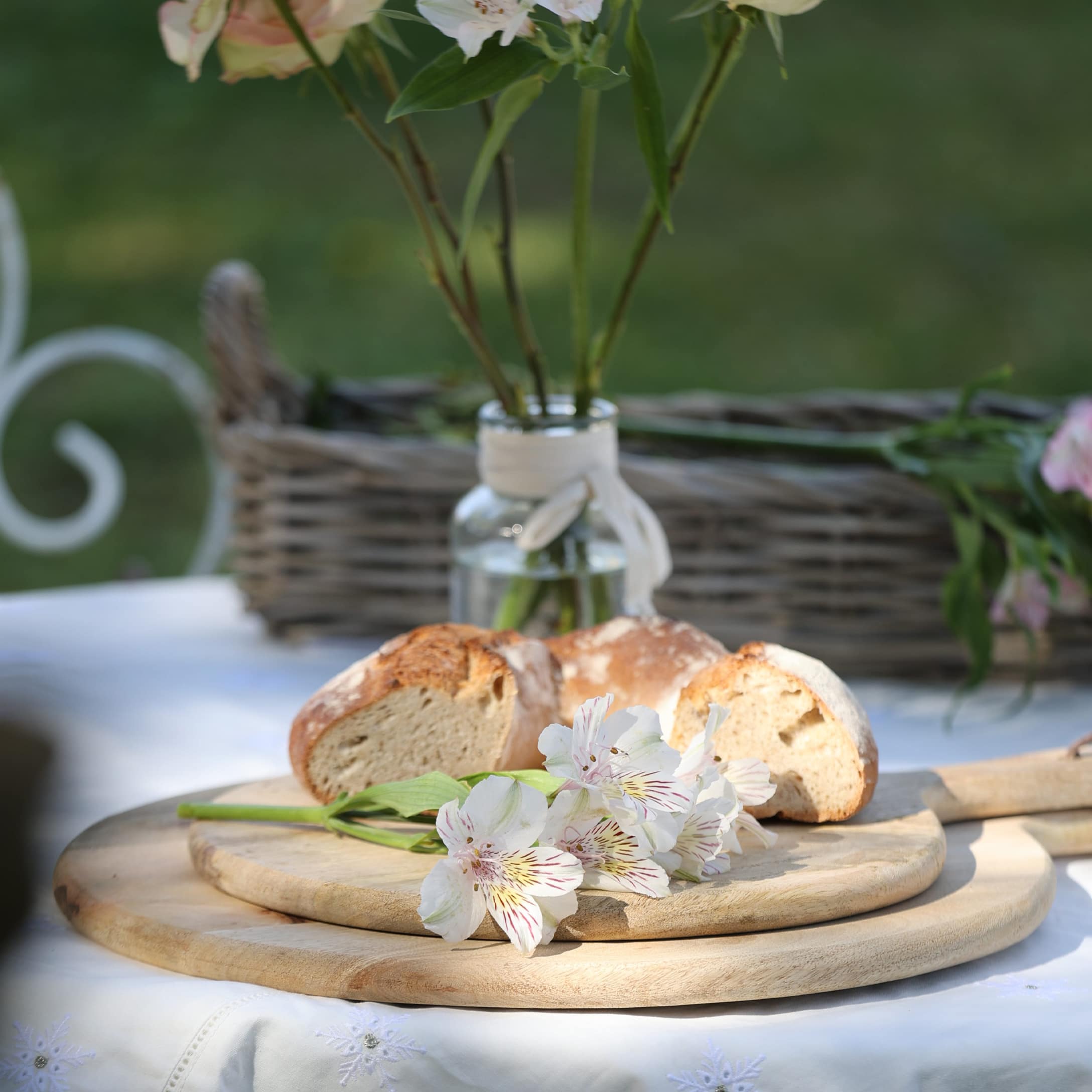 Planche à découper en bois avec fleurs blanches et morceaux de pain sur nappe blanche en extérieur