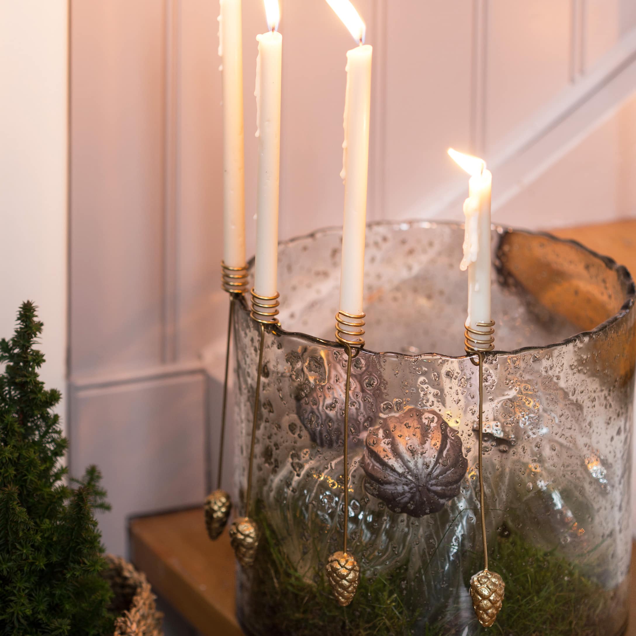 Bougeoir en verre avec bougies blanches et décorations en forme de pommes de pin dorées